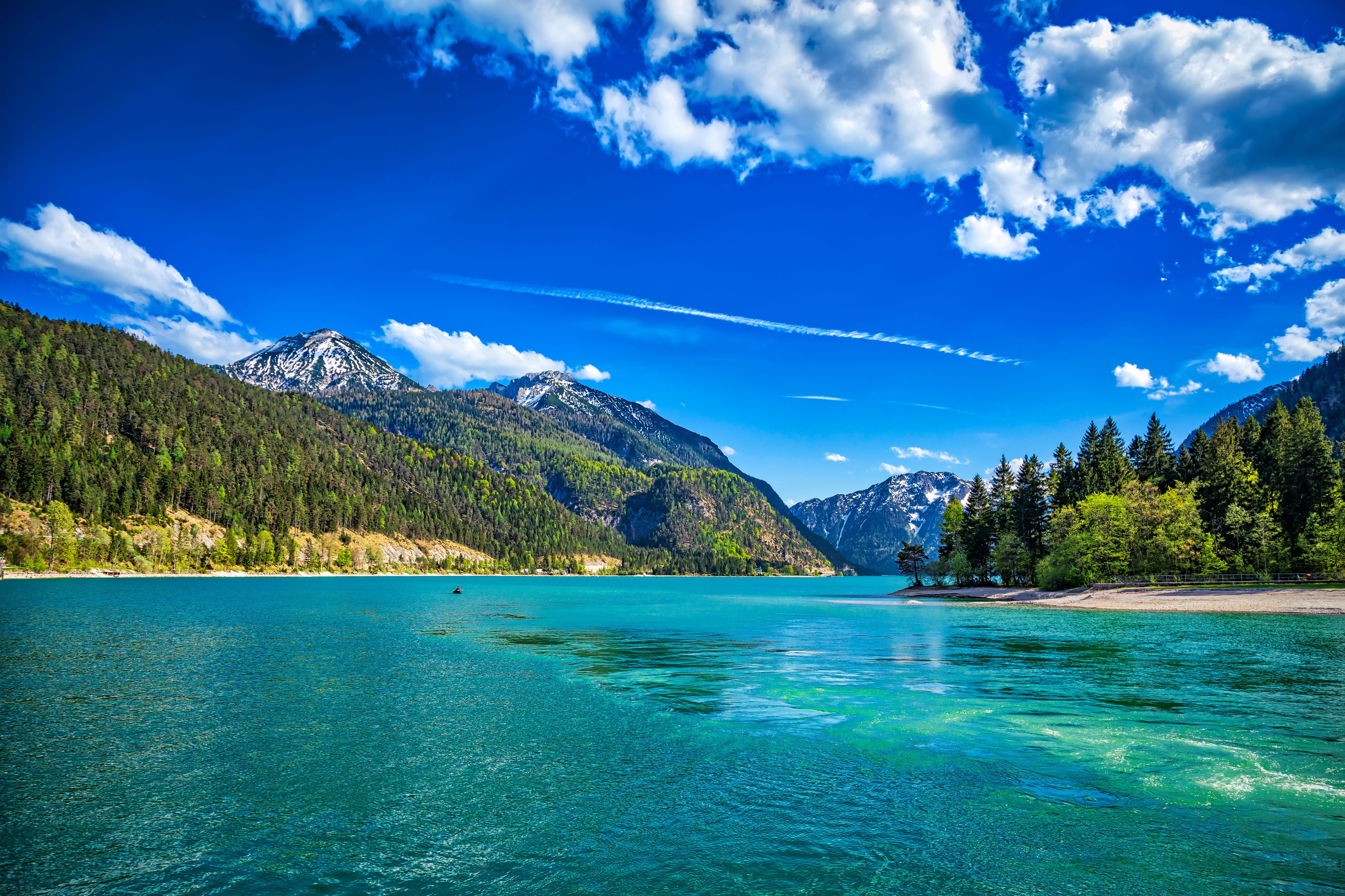 Panoramablick auf den türkisblauen Achensee mit bewaldeten Alpen und teils schneebedeckten Bergen.