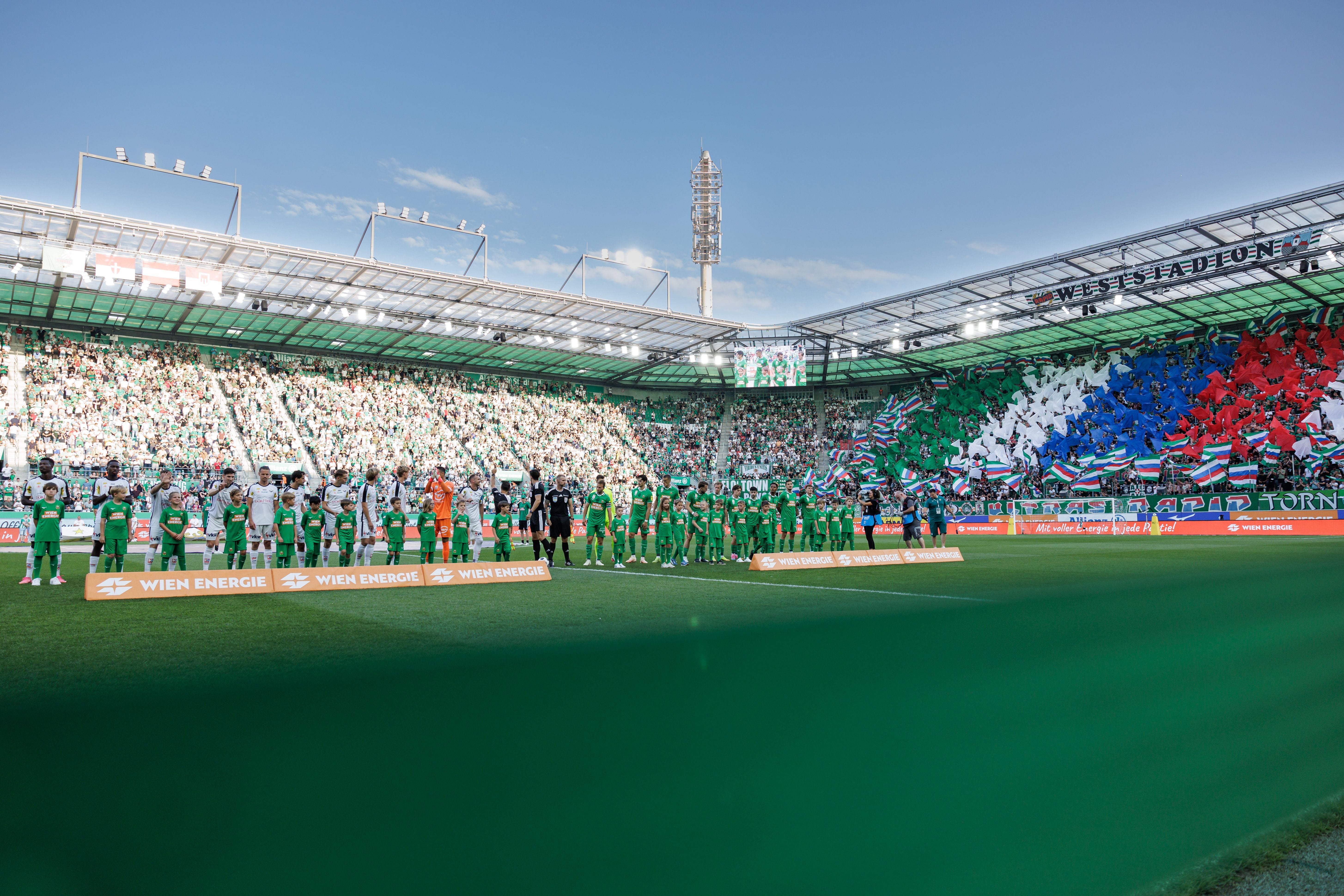Fußballteams stehen im Allianz Stadion, Rapid-Fans zeigen eine bunte Choreografie auf der Tribüne.
