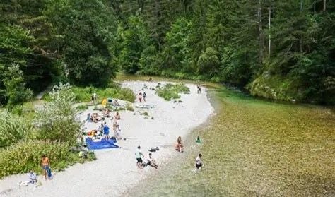 Menschen entspannen und baden an einem Kiesstrand im Höllental an einem klaren Fluss.