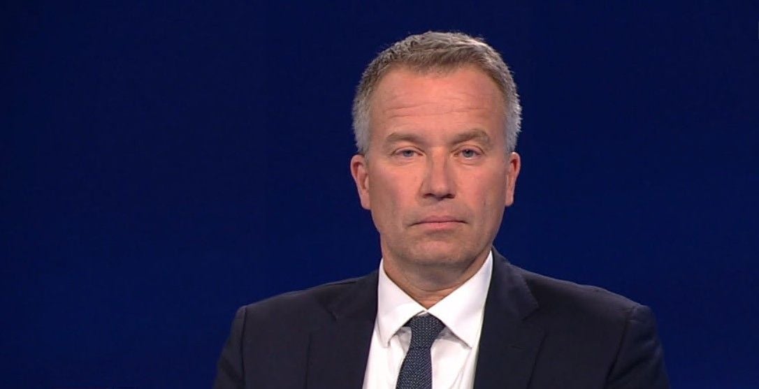 Mann im Anzug vor blauem Hintergrund, schaut ernst in die Kamera.