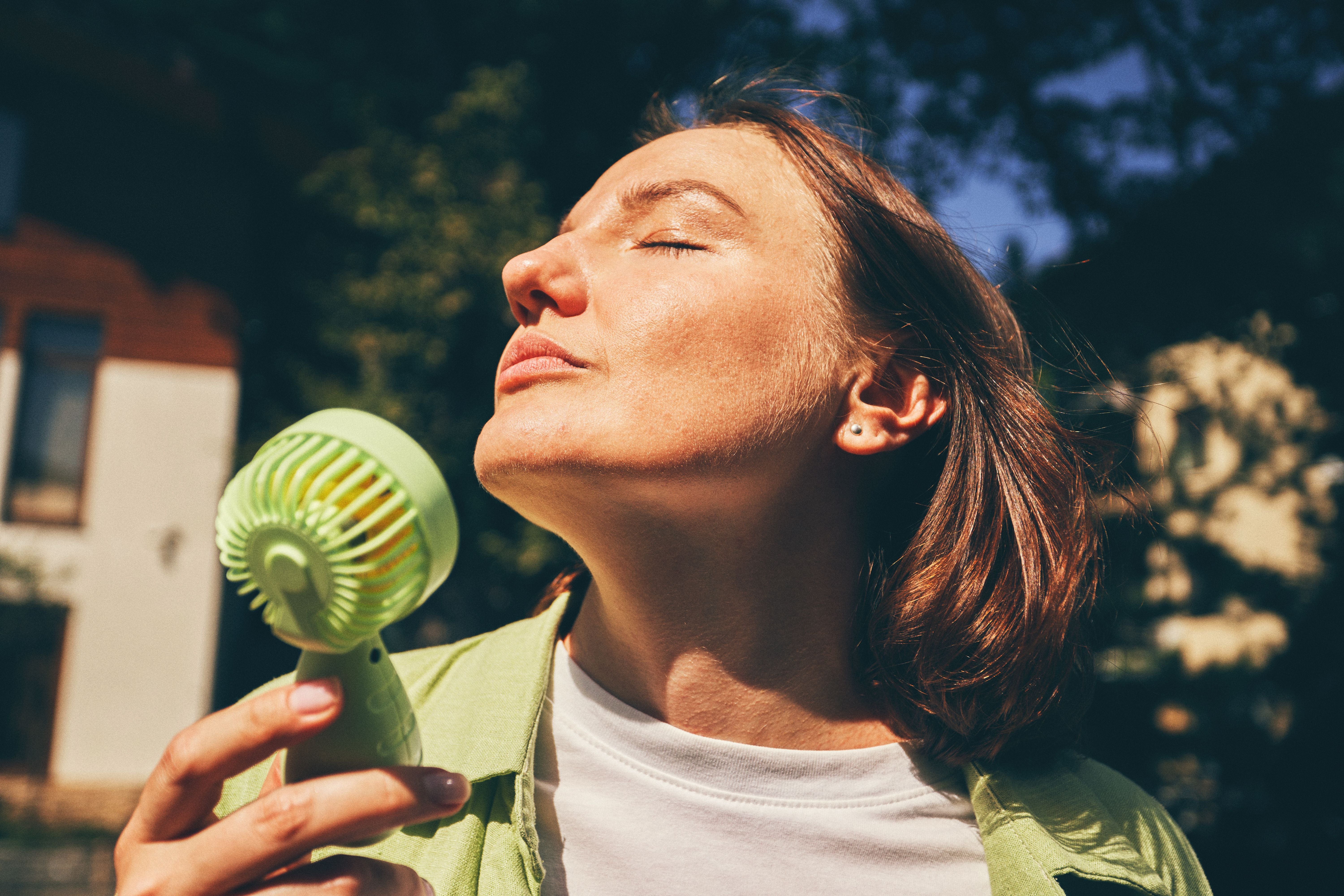 Frau genießt draußen an einem sonnigen Tag die kühle Brise eines grünen Handventilators.