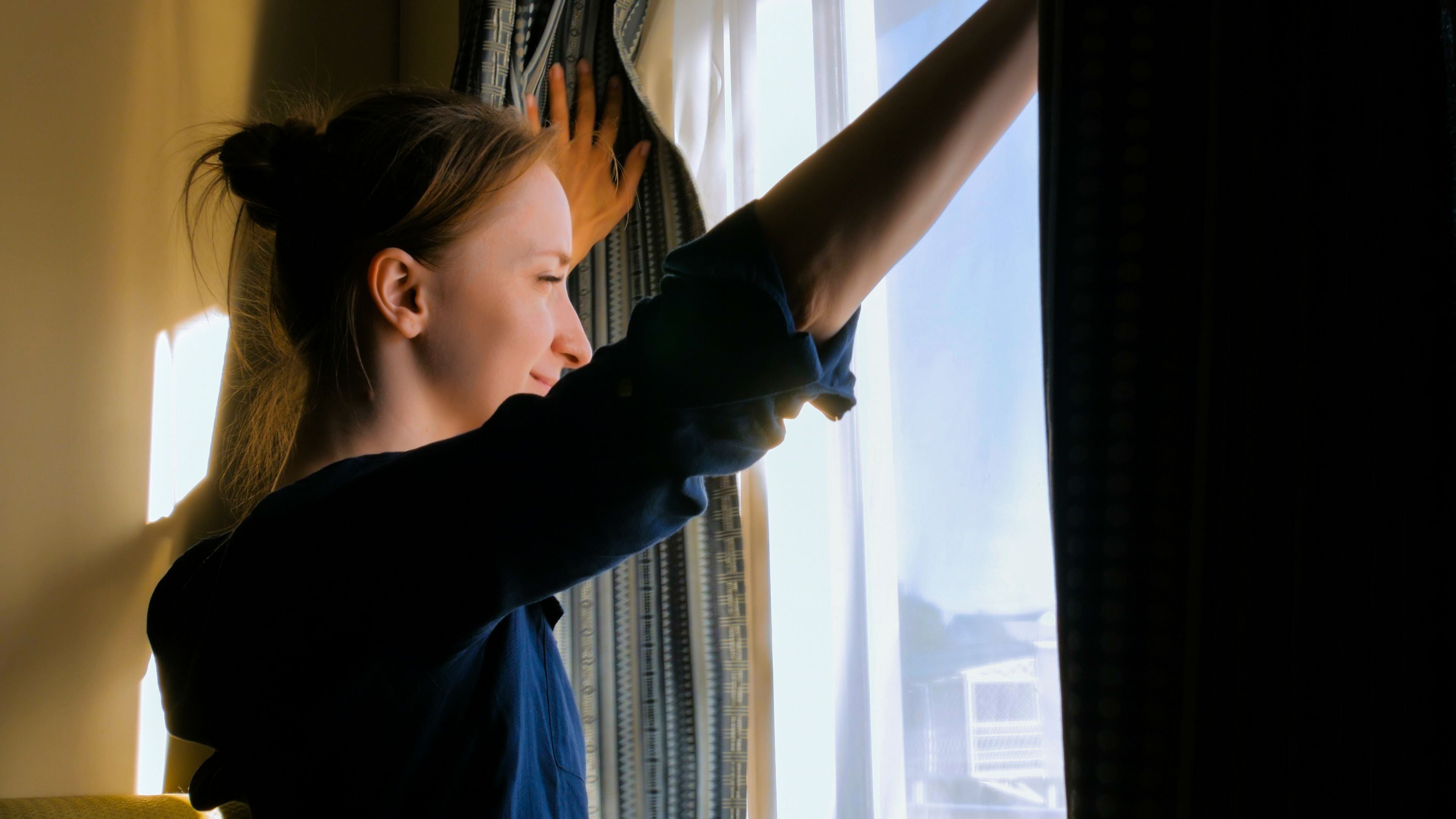 Frau öffnet morgens glücklich Vorhänge und schaut aus dem Fenster einer Schiffskabine.