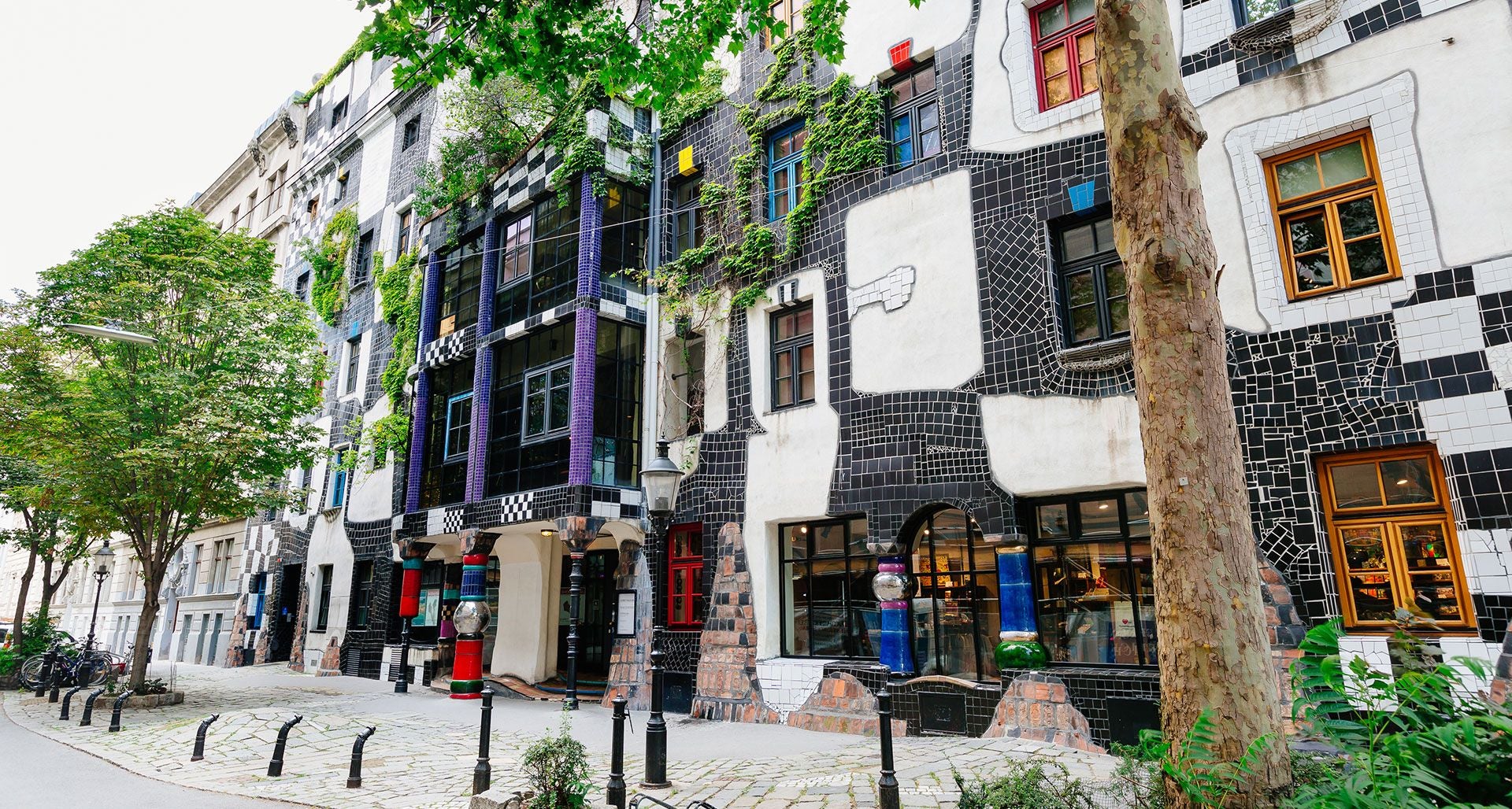 Fassade des KunstHausWien mit bunten, unregelmäßigen Fliesen und begrünten Bereichen.