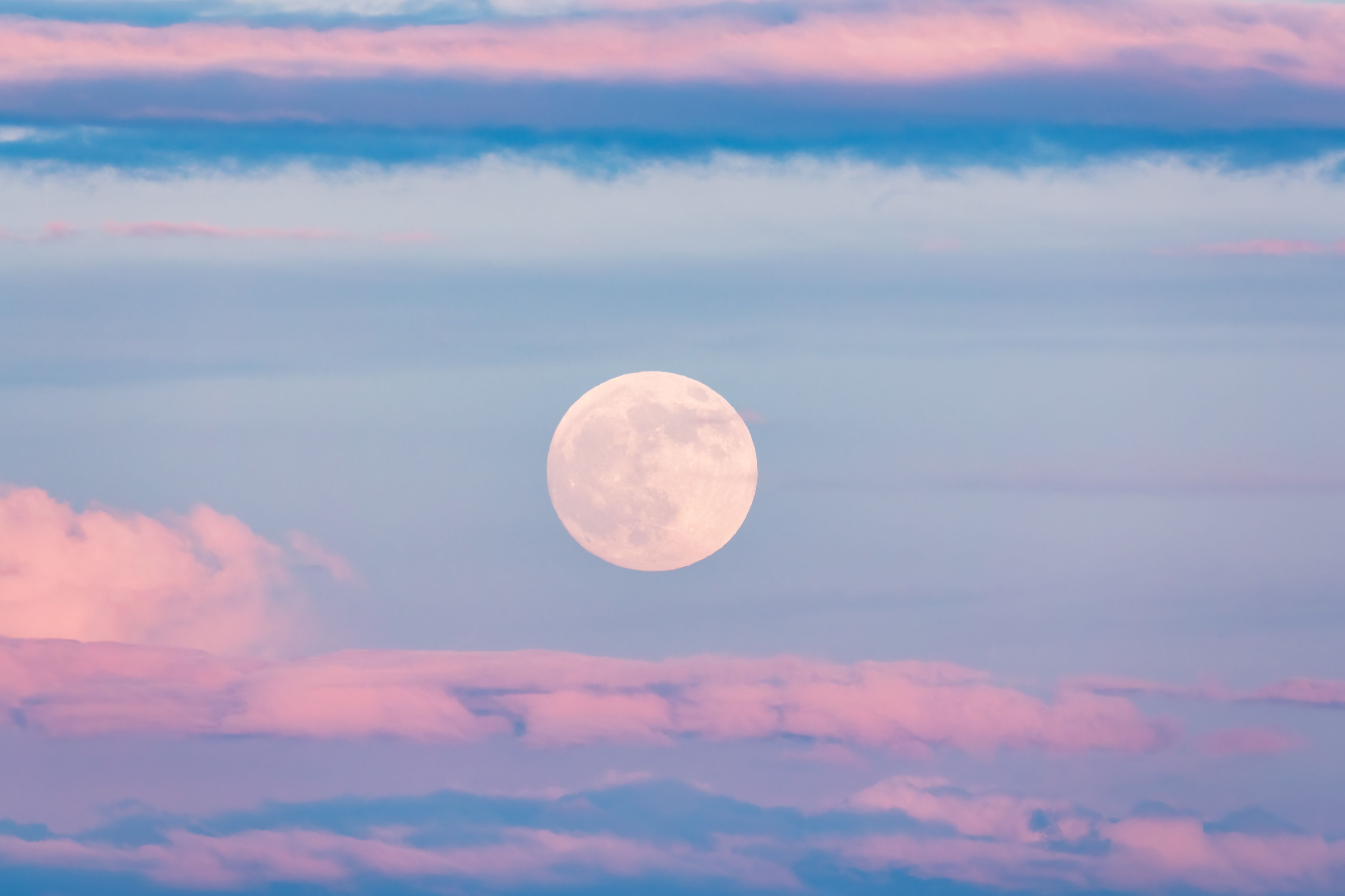 Vollmond am Himmel mit rosa-blauen Wolken bei Sonnenuntergang.