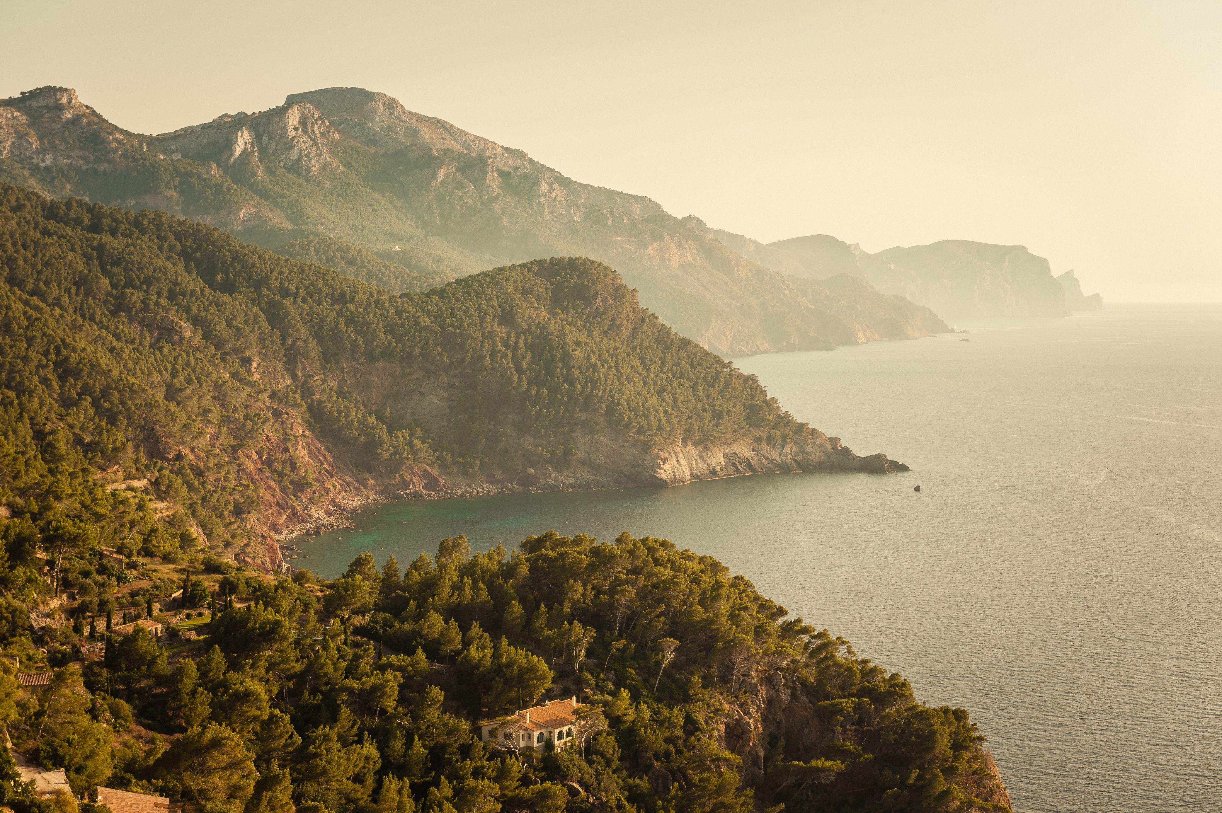 Küste mit bewaldeten Bergen im Sonnenlicht, Blick auf das ruhige Meer.