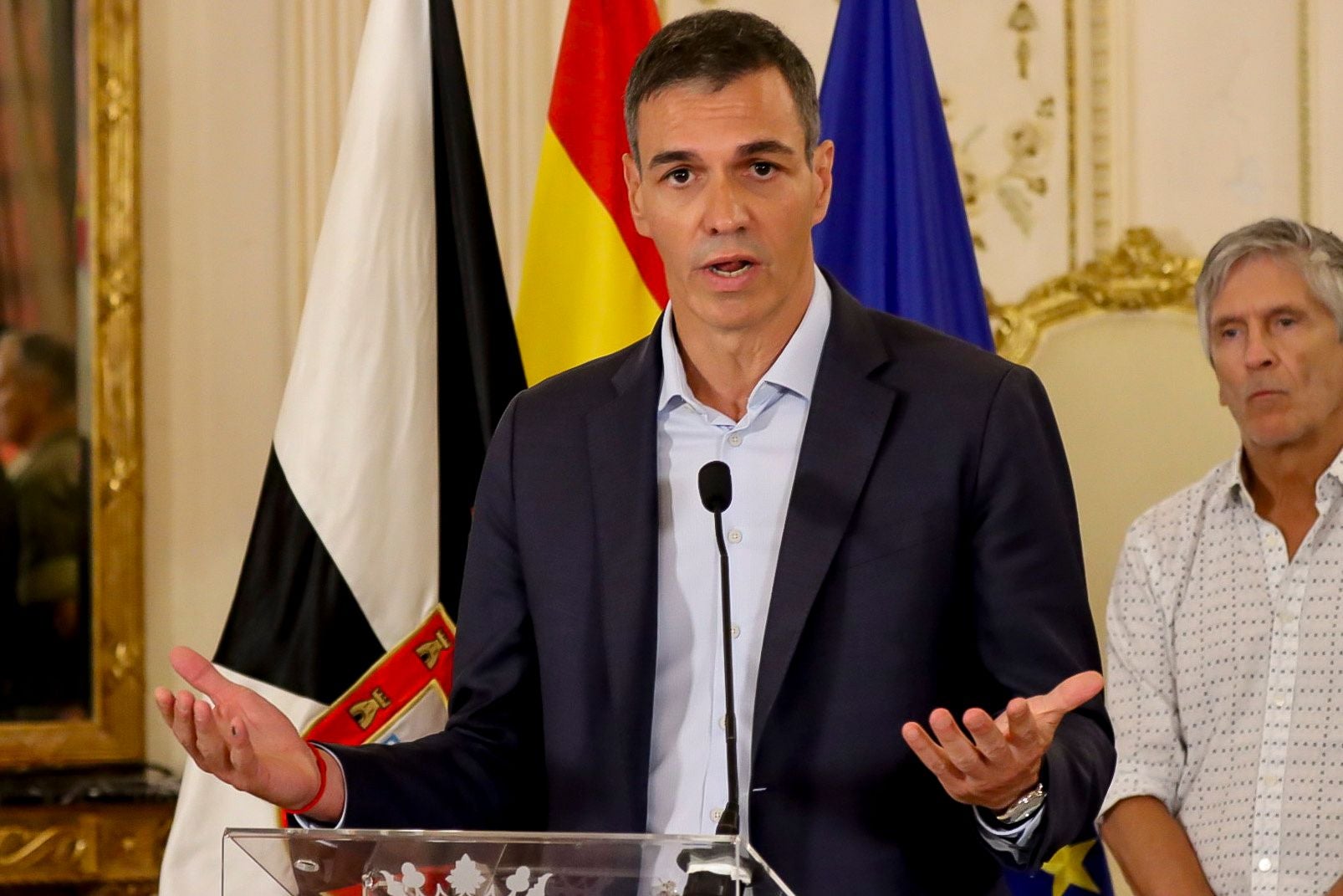 Ein Mann hält eine Pressekonferenz, im Hintergrund sind Flaggen zu sehen.