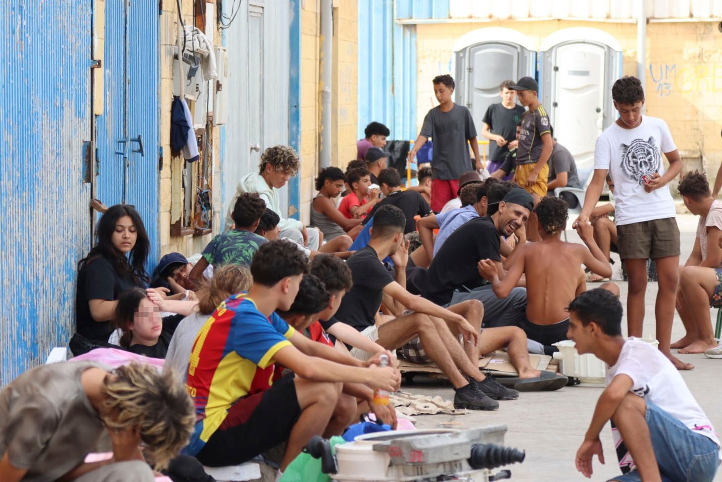 Viele junge Migranten sitzen auf einer Straße in Ceuta, einige unterhalten sich, andere ruhen sich aus.