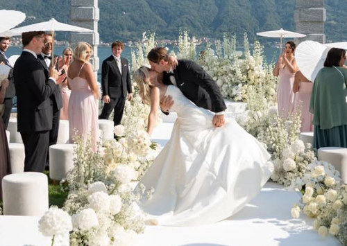 Brautpaar küsst sich bei einer Hochzeit im Freien, umgeben von weißen Blumen und Gästen.