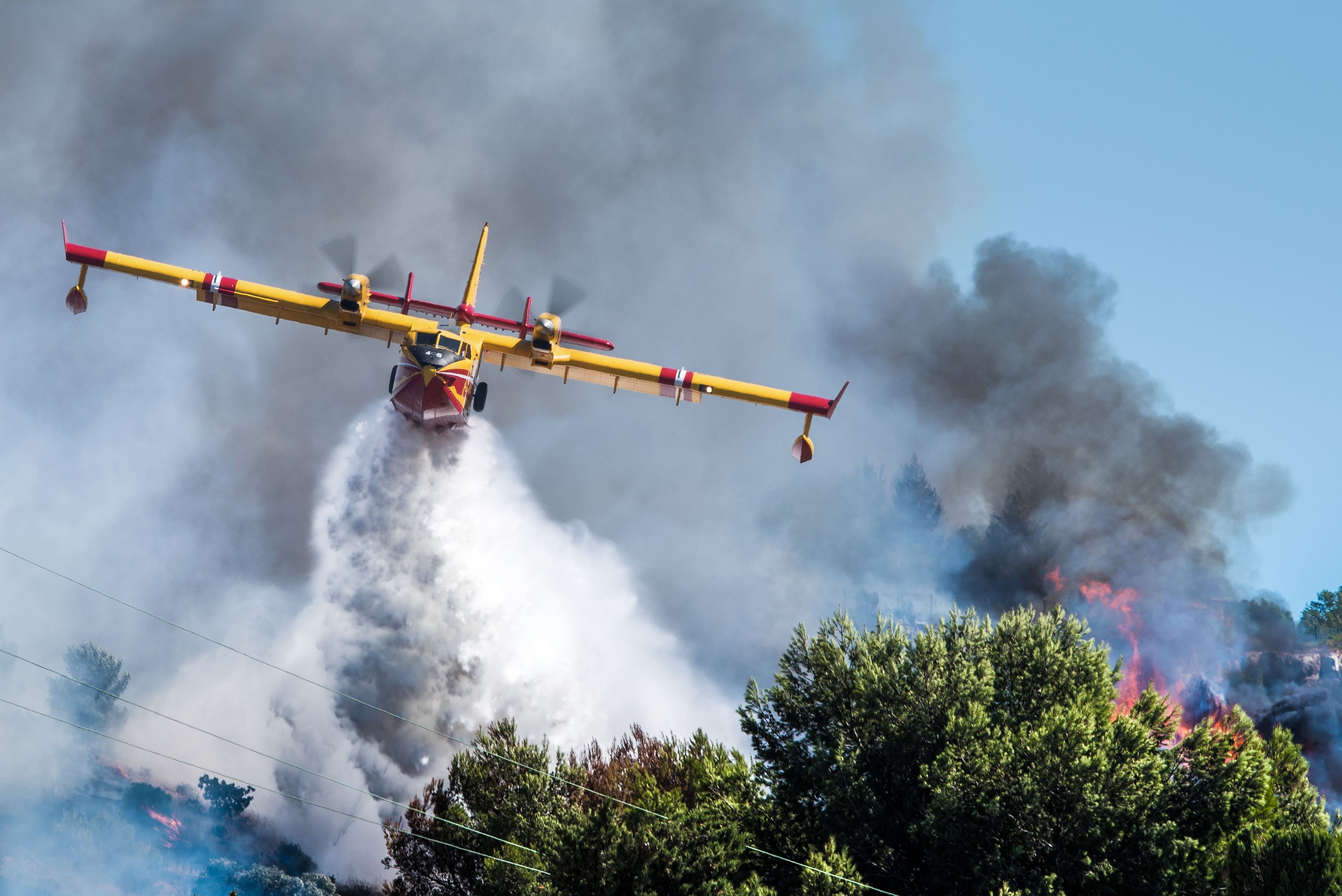 Ein Löschflugzeug wirft Wasser über einen brennenden Wald, starker Rauch steigt auf.