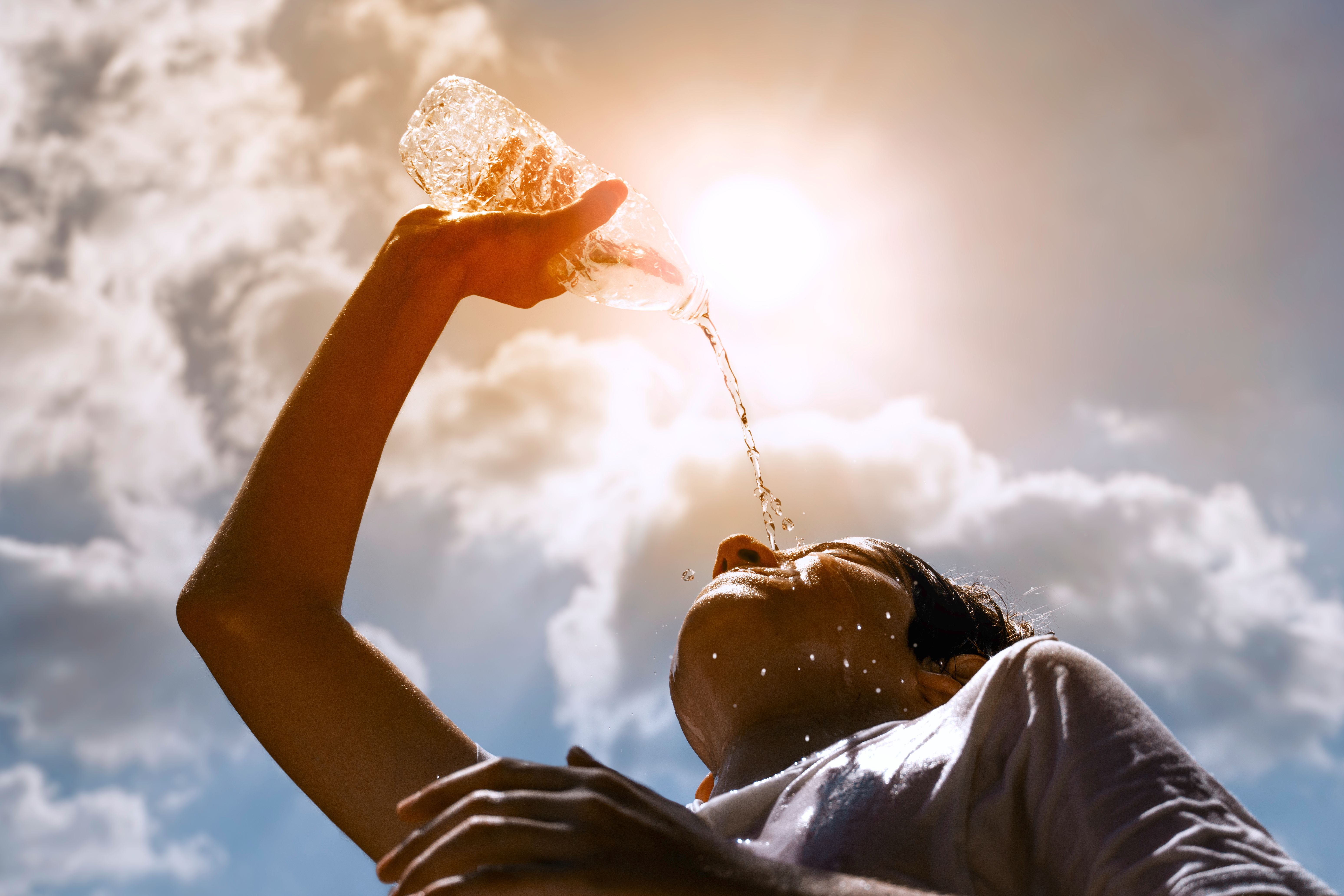 Frau trinkt Wasser aus Plastikflasche in der Sonne, Wasserspritzer auf ihrem Gesicht.