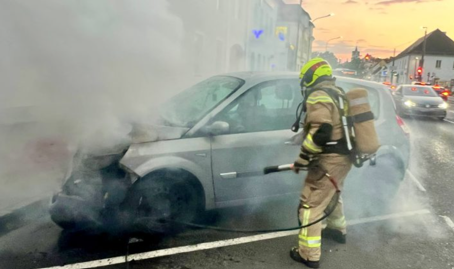 Feuerwehrmann löscht ein brennendes Auto auf einer Straße in Ebreichsdorf.