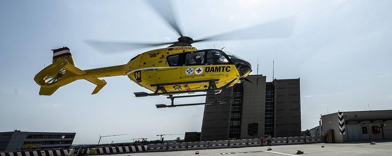 Gelber Rettungshubschrauber startet auf dem Dach eines Gebäudes, Hintergrund mit Hochhaus.