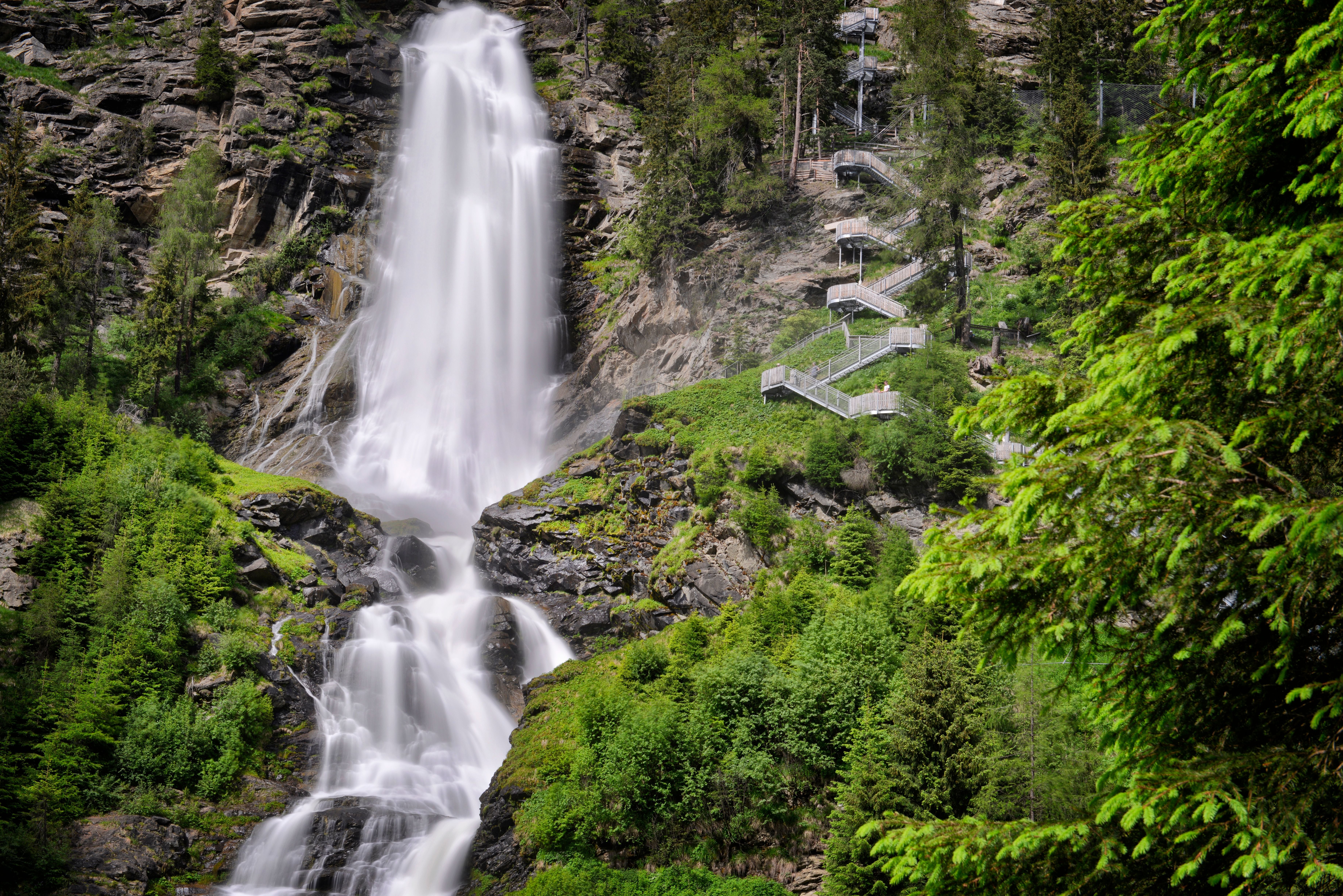 Wasserfall Stuibenfall in Tirol stürzt neben einer steilen Treppe durch üppigen grünen Wald.