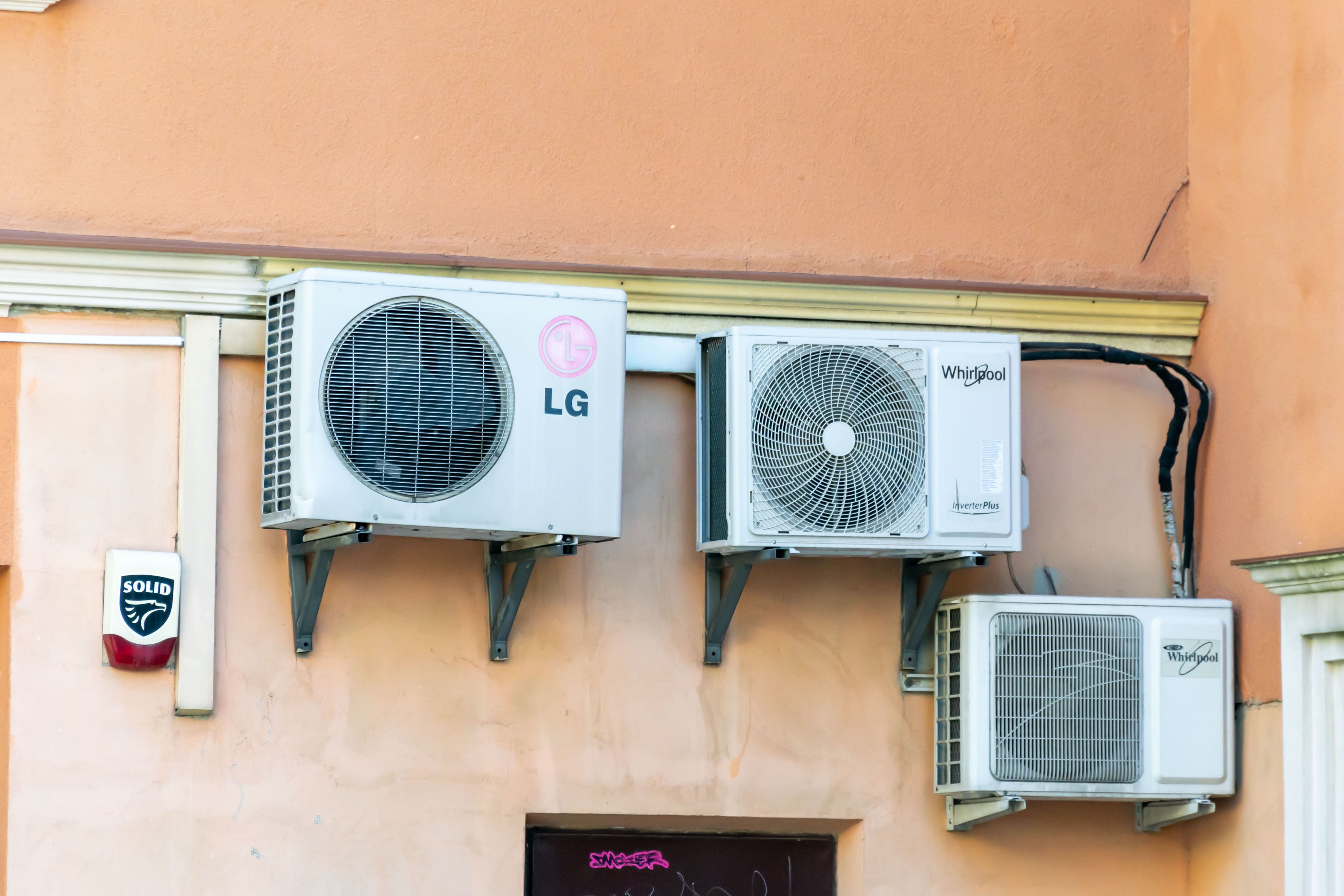 Drei Außenklimageräte von LG und Whirlpool an einer Gebäudewand montiert.