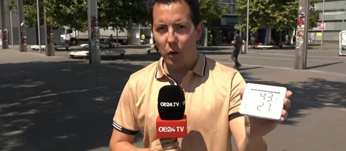 Ein Reporter hält ein OE24.TV-Mikrofon und ein Thermometer mit 43,1 Grad Celsius im Freien.