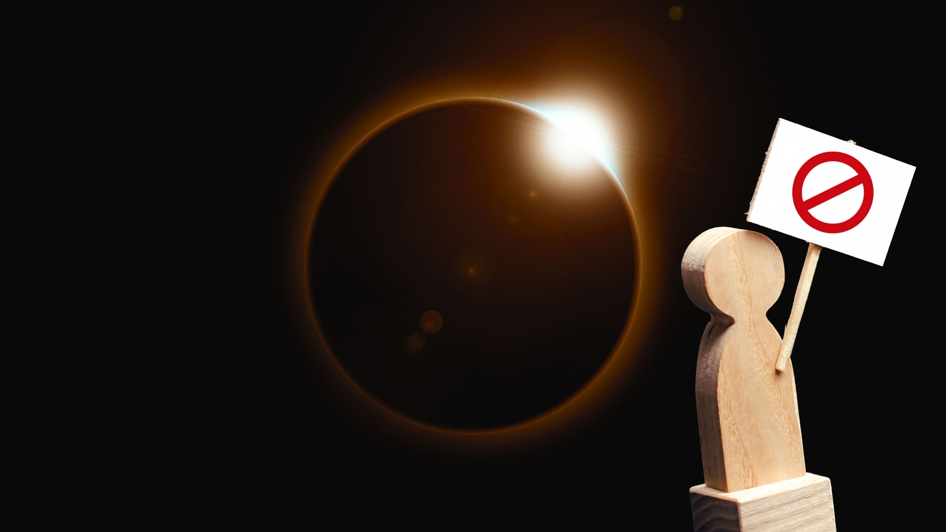 Holzfigur mit Verbotsschild vor einer Sonnenfinsternis auf schwarzem Hintergrund.