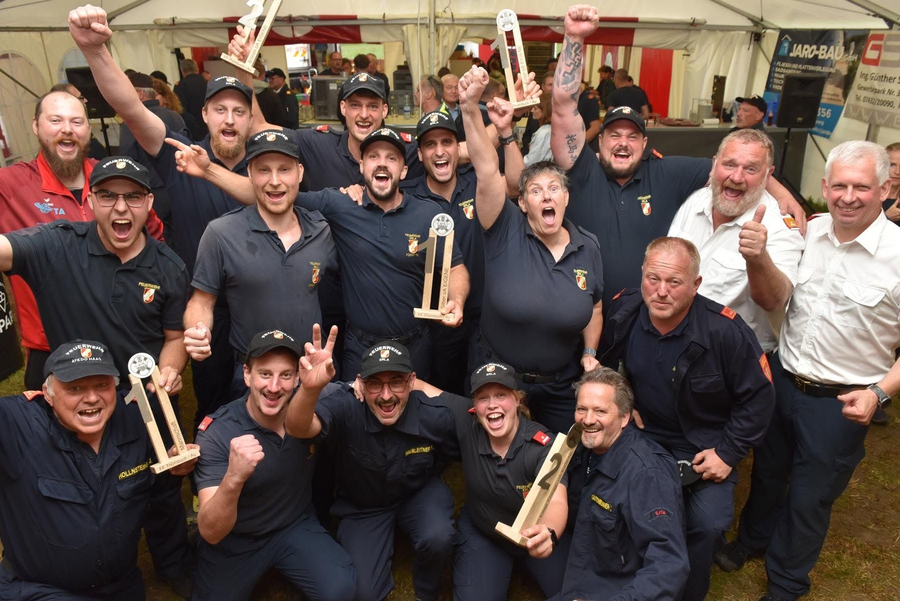 Gruppe jubelnder Feuerwehrleute mit Pokalen bei einem Festzelt-Wettbewerb in Ardagger.