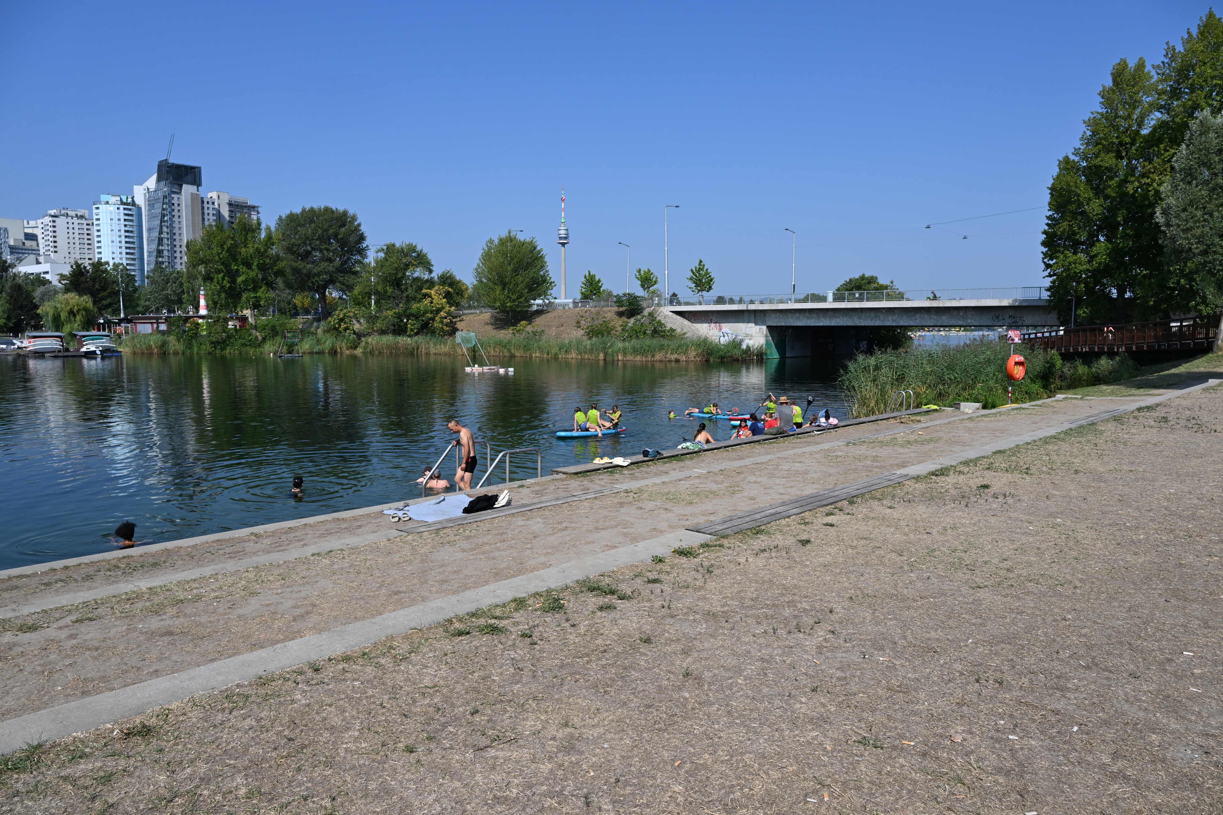 Menschen baden und entspannen an der ausgetrockneten Uferböschung der Alten Donau in Wien.