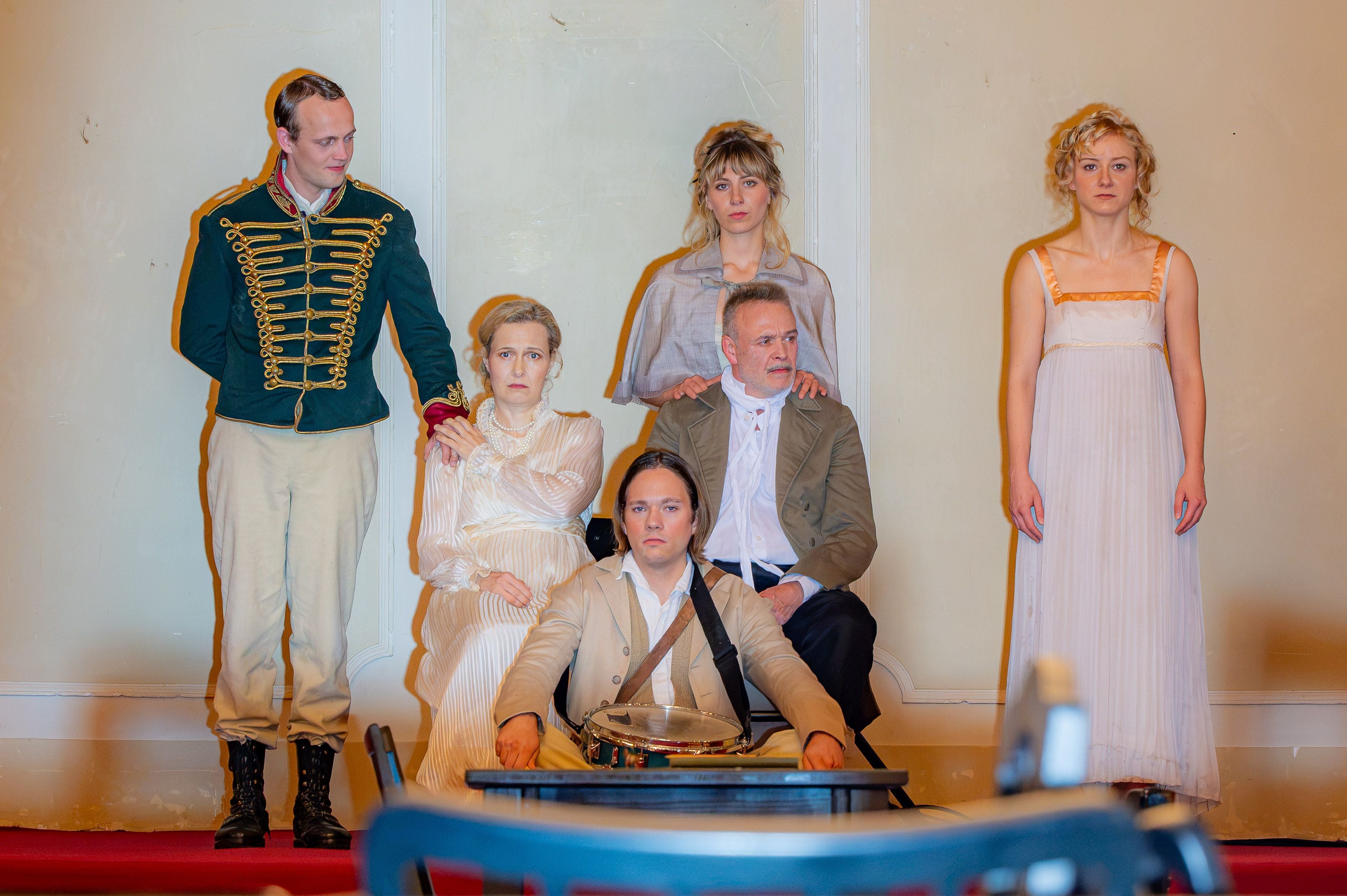 Fünf Menschen in historischen Kostümen posieren ernst bei einer Theaterprobe zu "Krieg und Frieden".