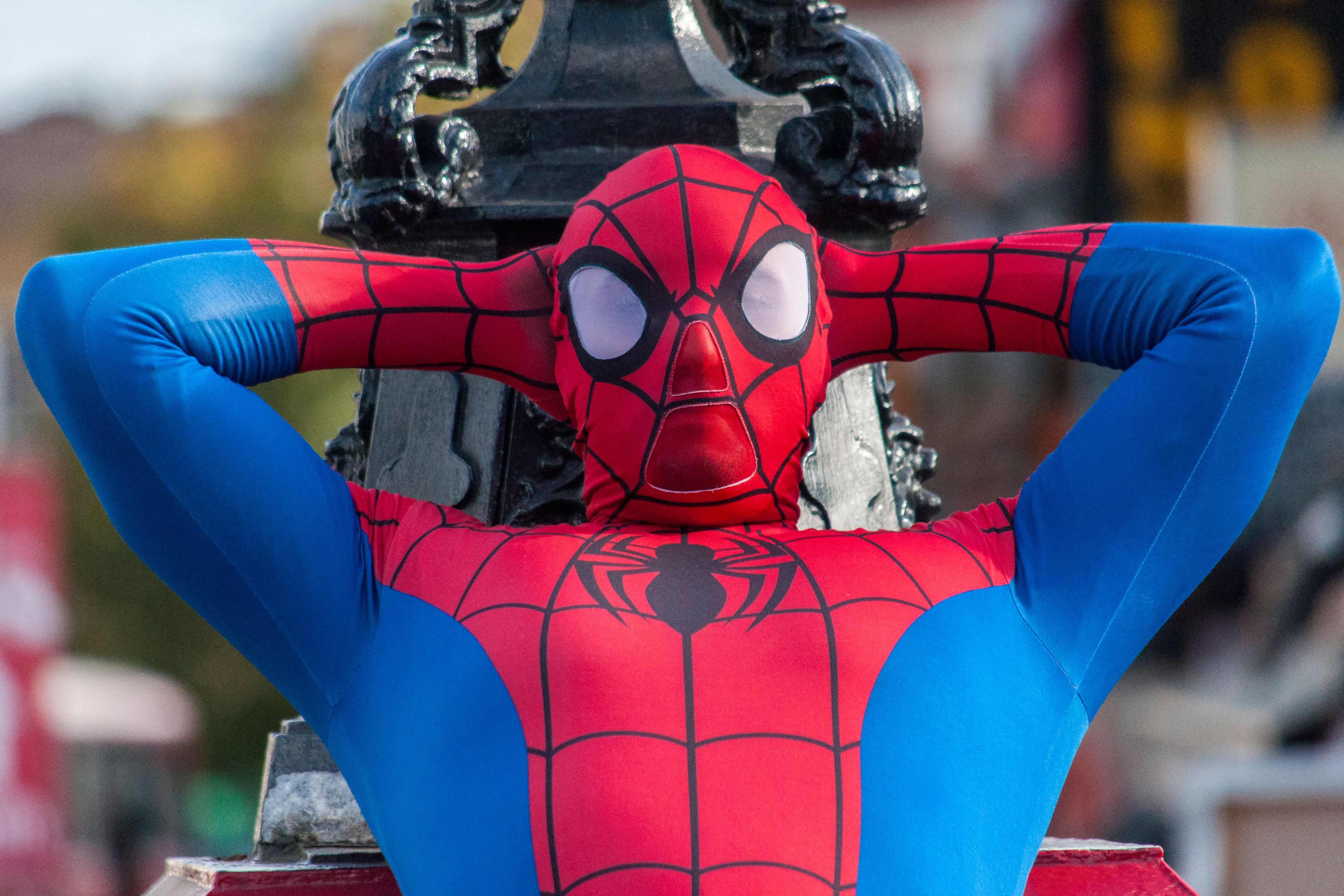 Person in Spiderman-Kostüm lehnt sich entspannt an eine Laterne in einer belebten Straße.