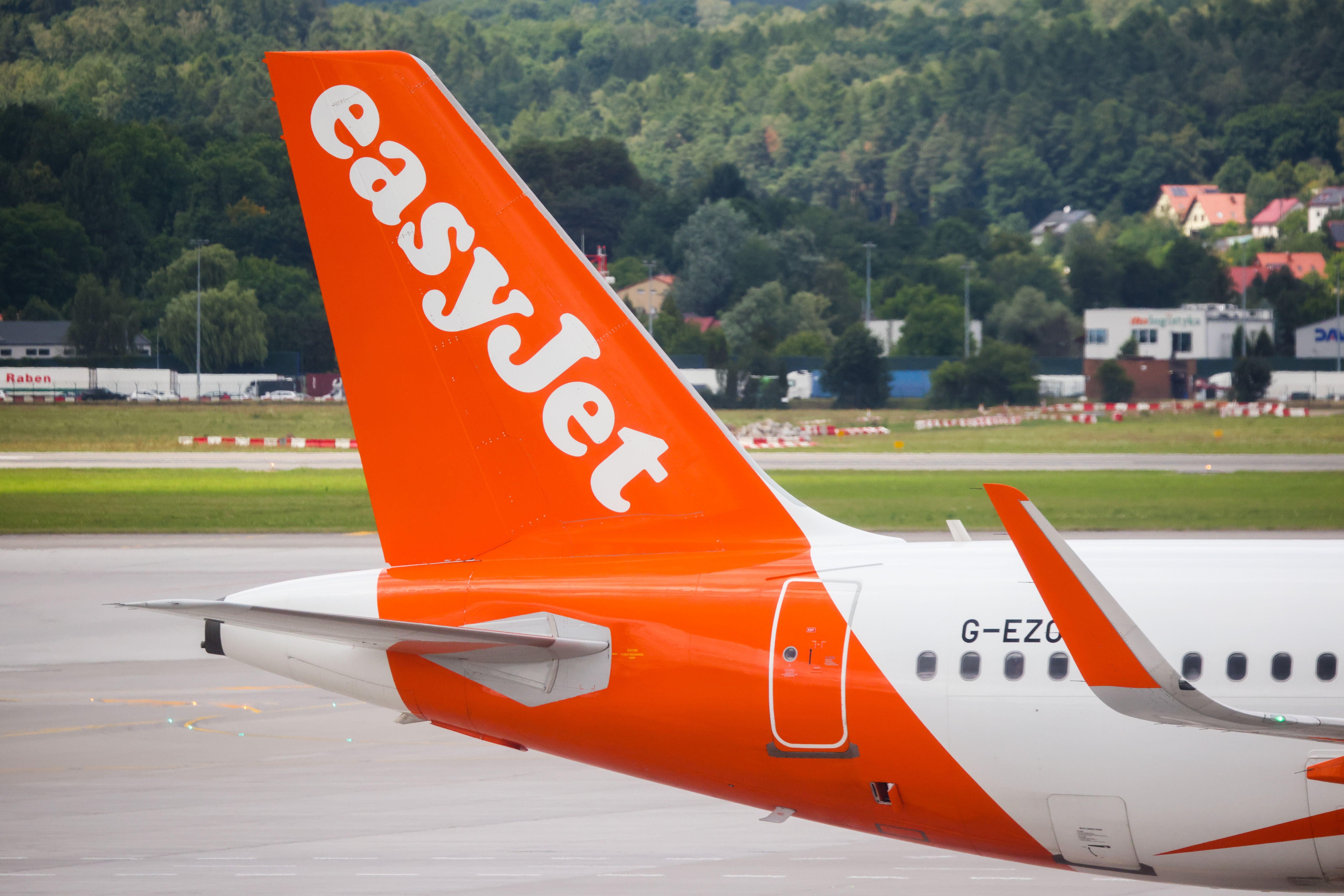 Orange Leitwerk eines easyJet-Flugzeugs am Flughafen Krakau mit Gebäuden im Hintergrund.