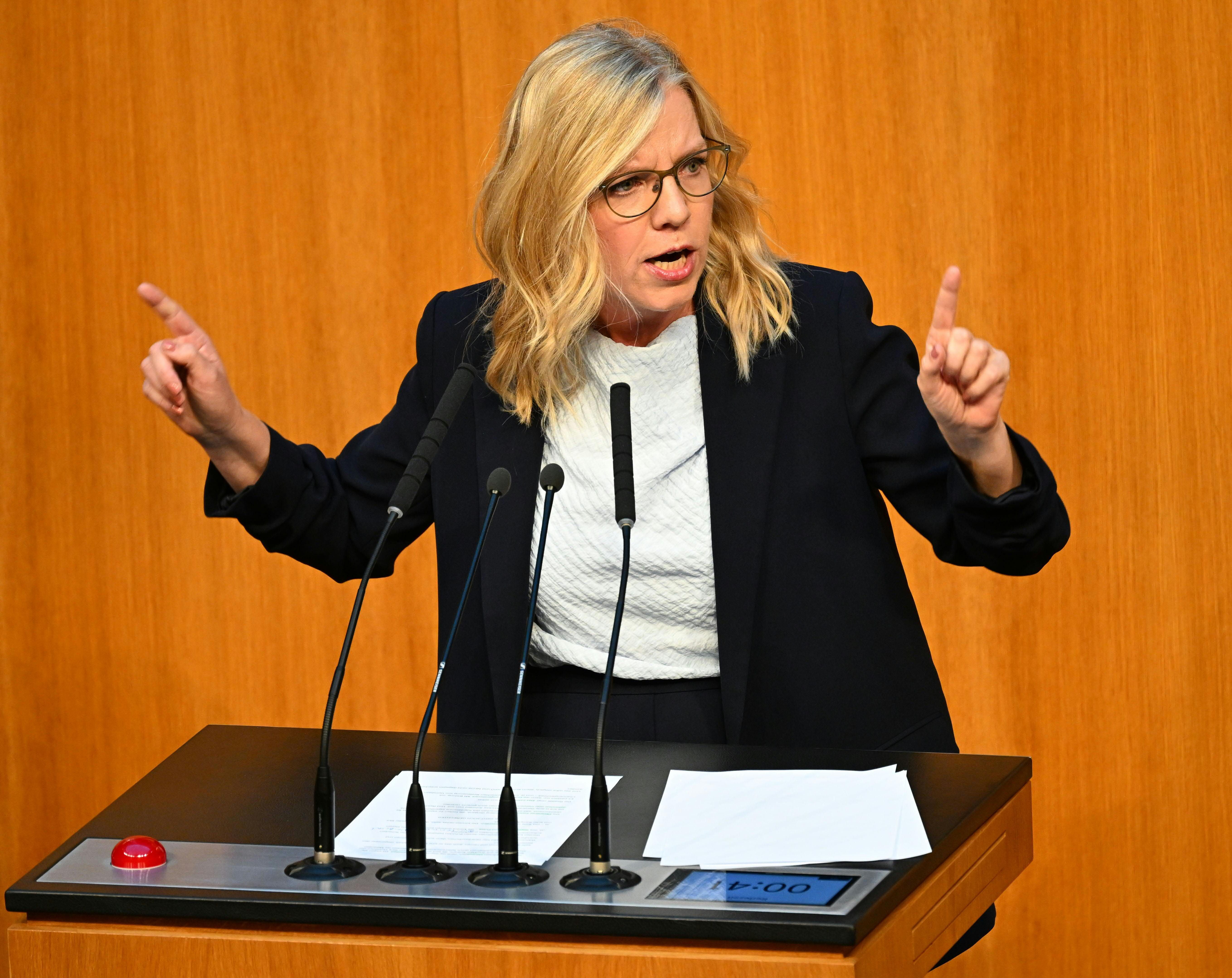Frau spricht gestikulierend an einem Rednerpult im Parlament vor Holzvertäfelung.