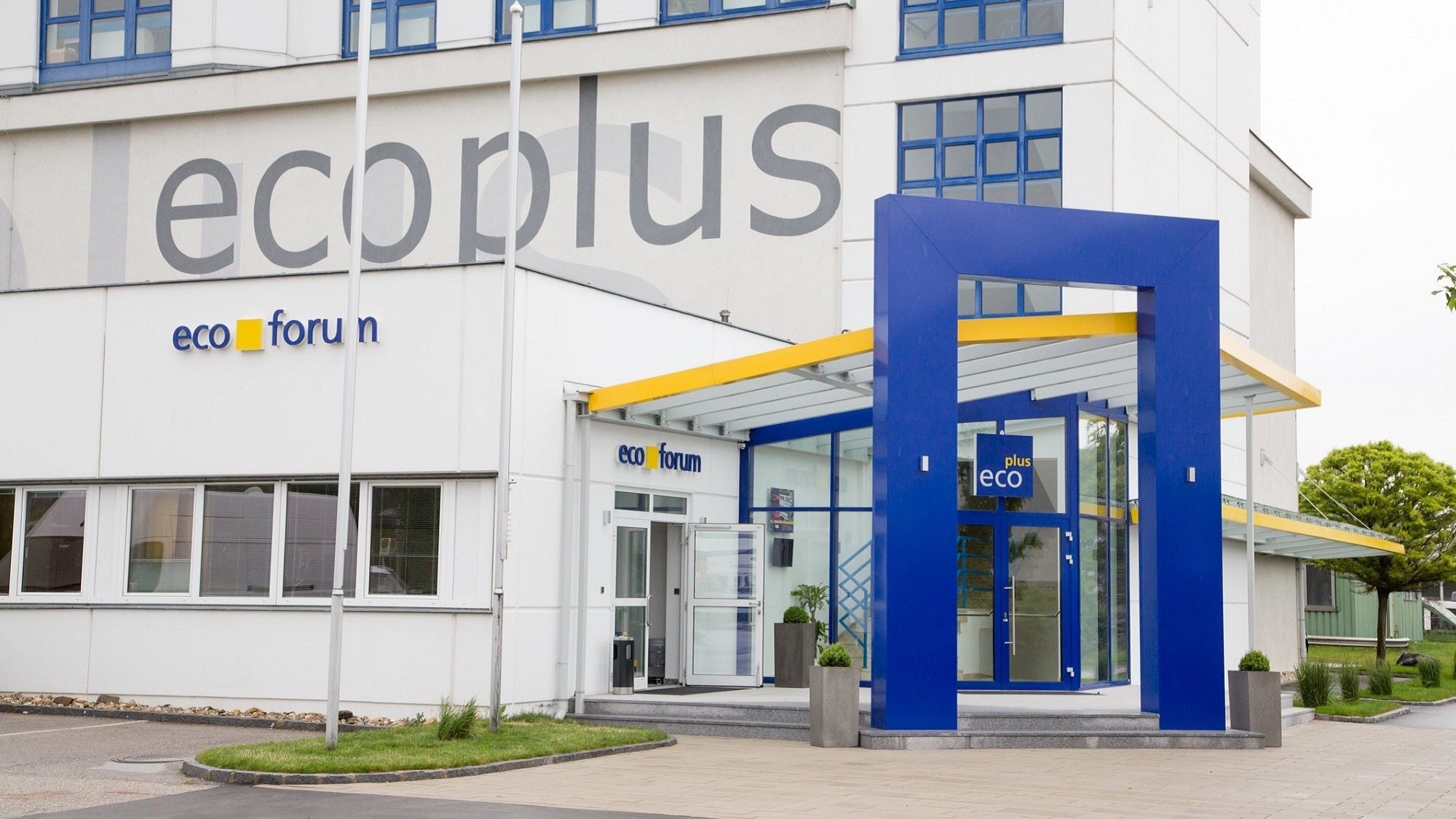Eingang der ecoplus-Zentrale mit blau-gelber Überdachung und großem Firmenlogo.