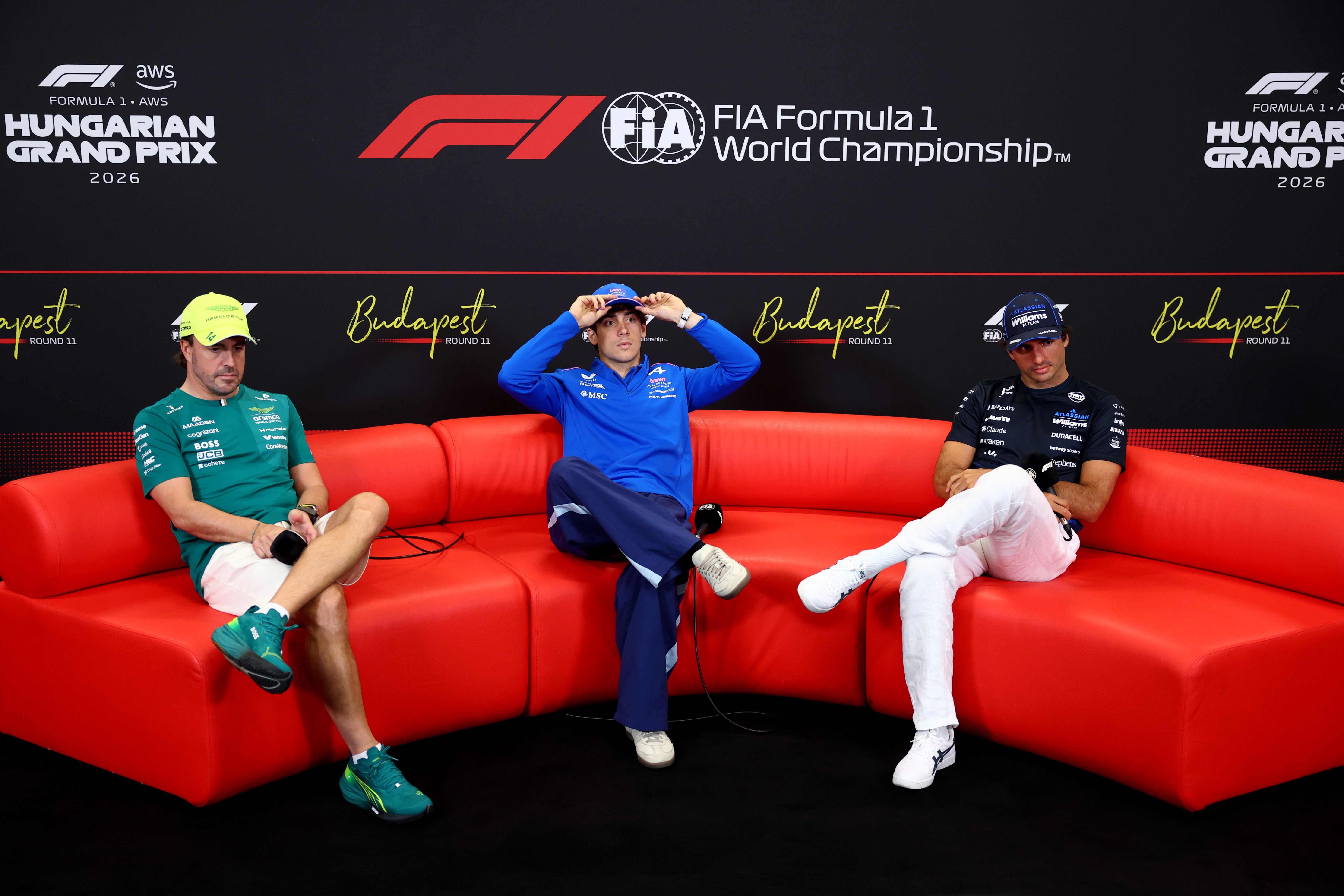 Drei Formel-1-Fahrer sitzen während einer Pressekonferenz auf einem roten Sofa in Budapest.