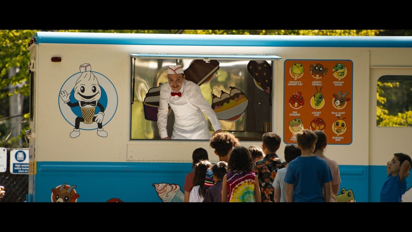 Kinder stehen vor einem Eiswagen, aus dem ein Eisverkäufer in Uniform blickt.