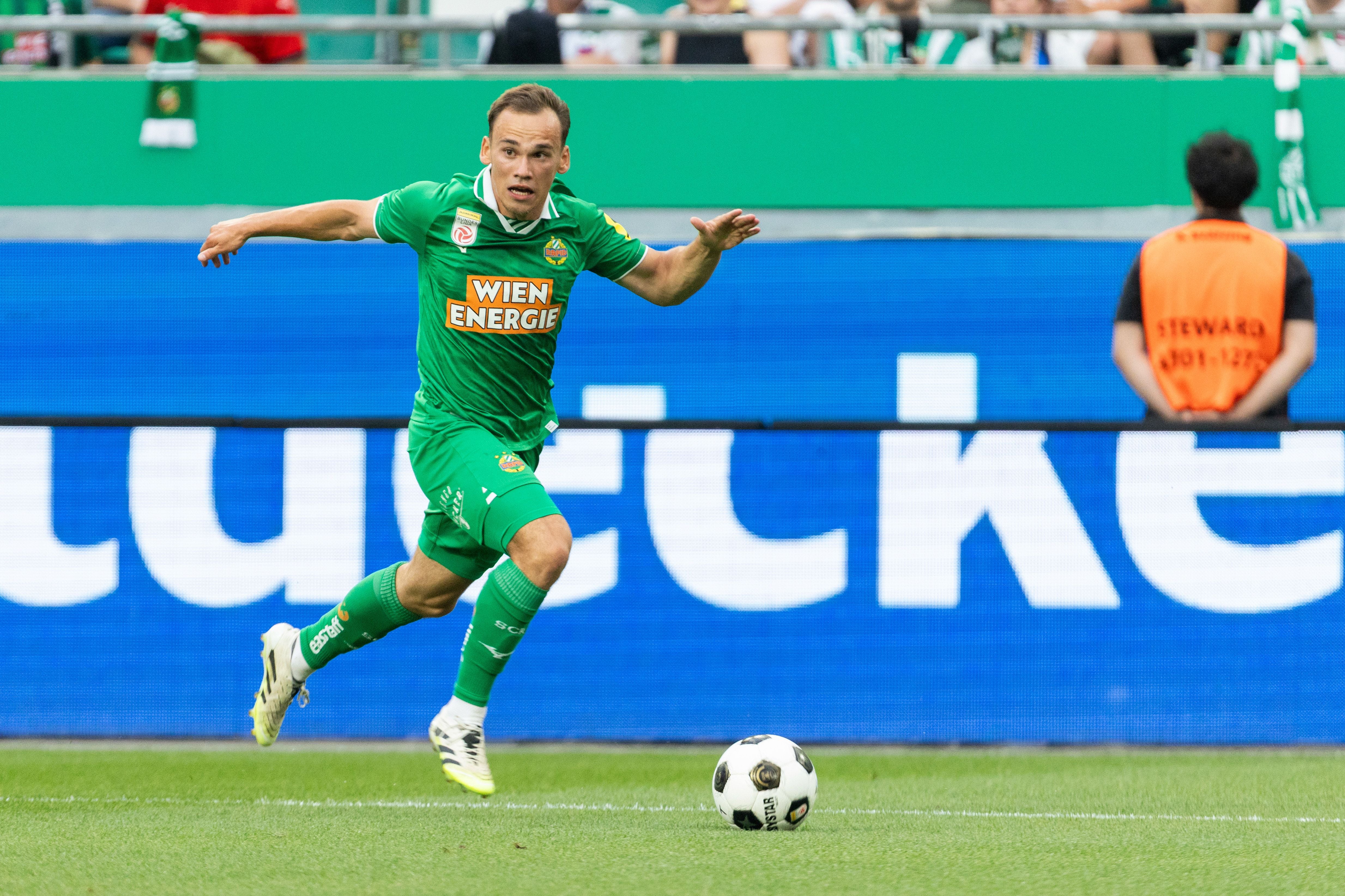 Ein Rapid-Wien-Spieler im grünen Trikot läuft mit dem Ball auf dem Fußballfeld.