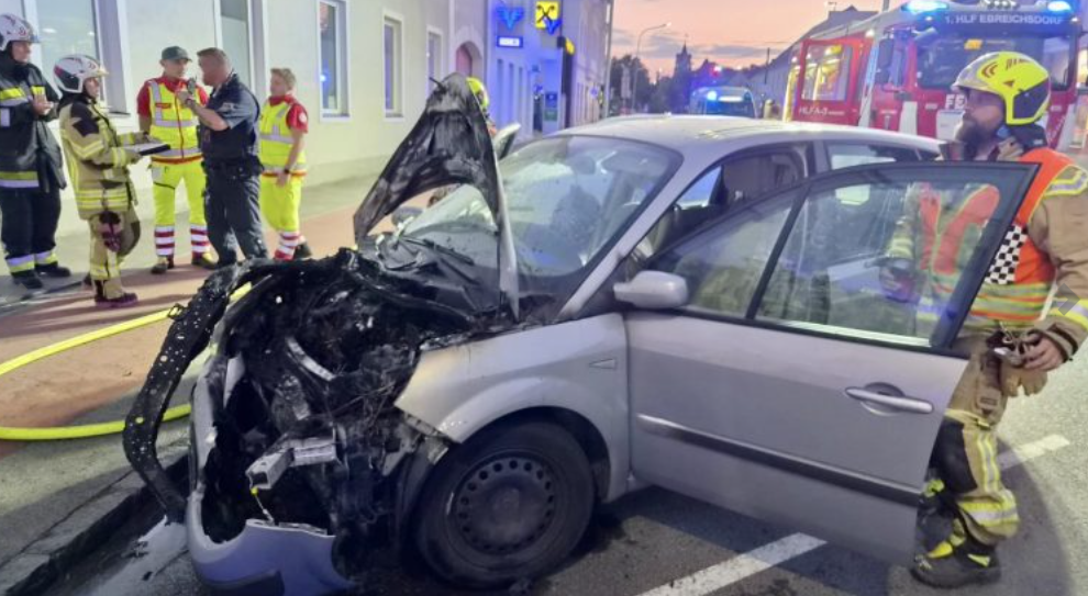 Feuerwehr löscht ein ausgebranntes Auto am Straßenrand in Ebreichsdorf bei Dämmerung.
