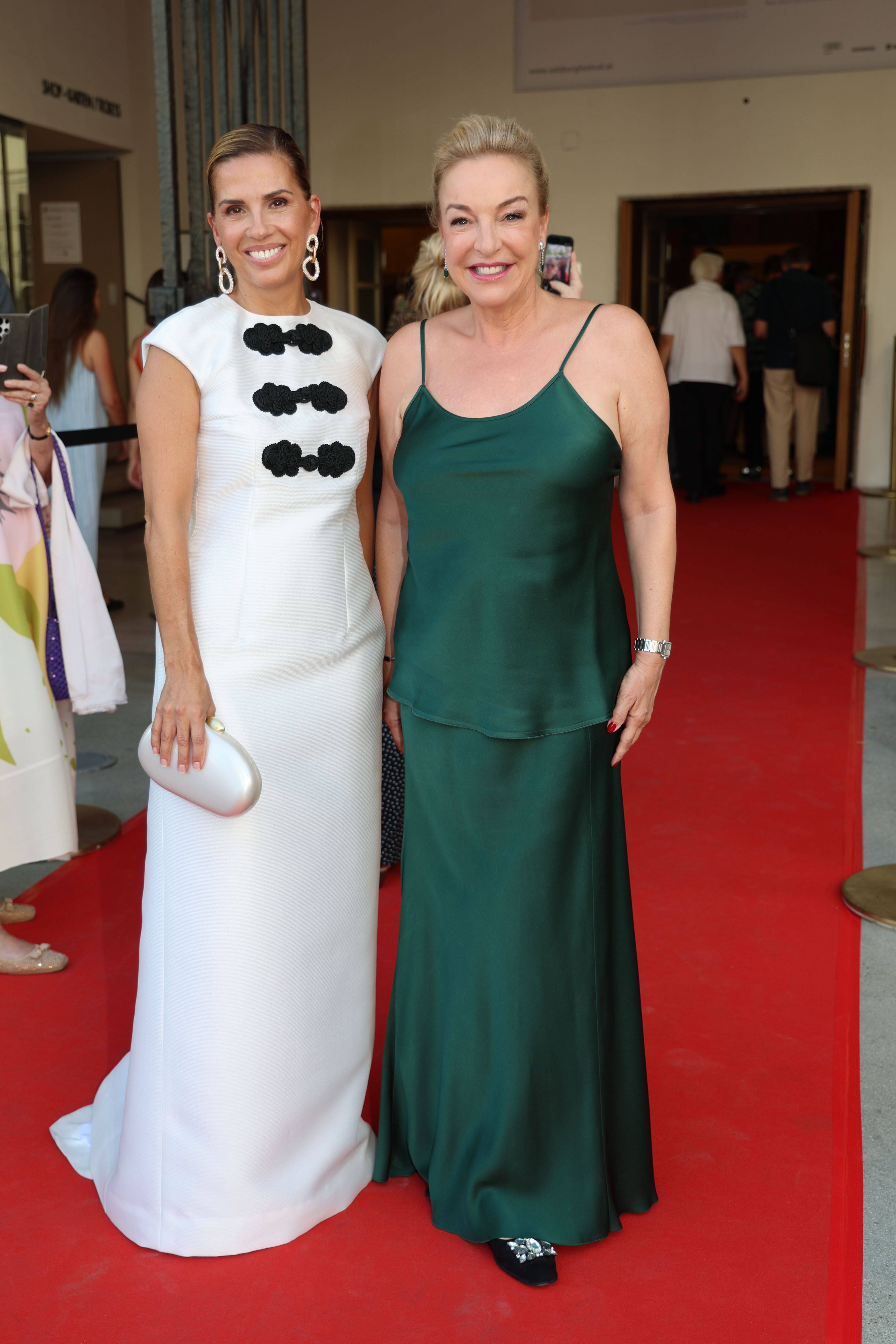 Zwei elegant gekleidete Frauen posieren auf rotem Teppich bei den Salzburger Festspielen.