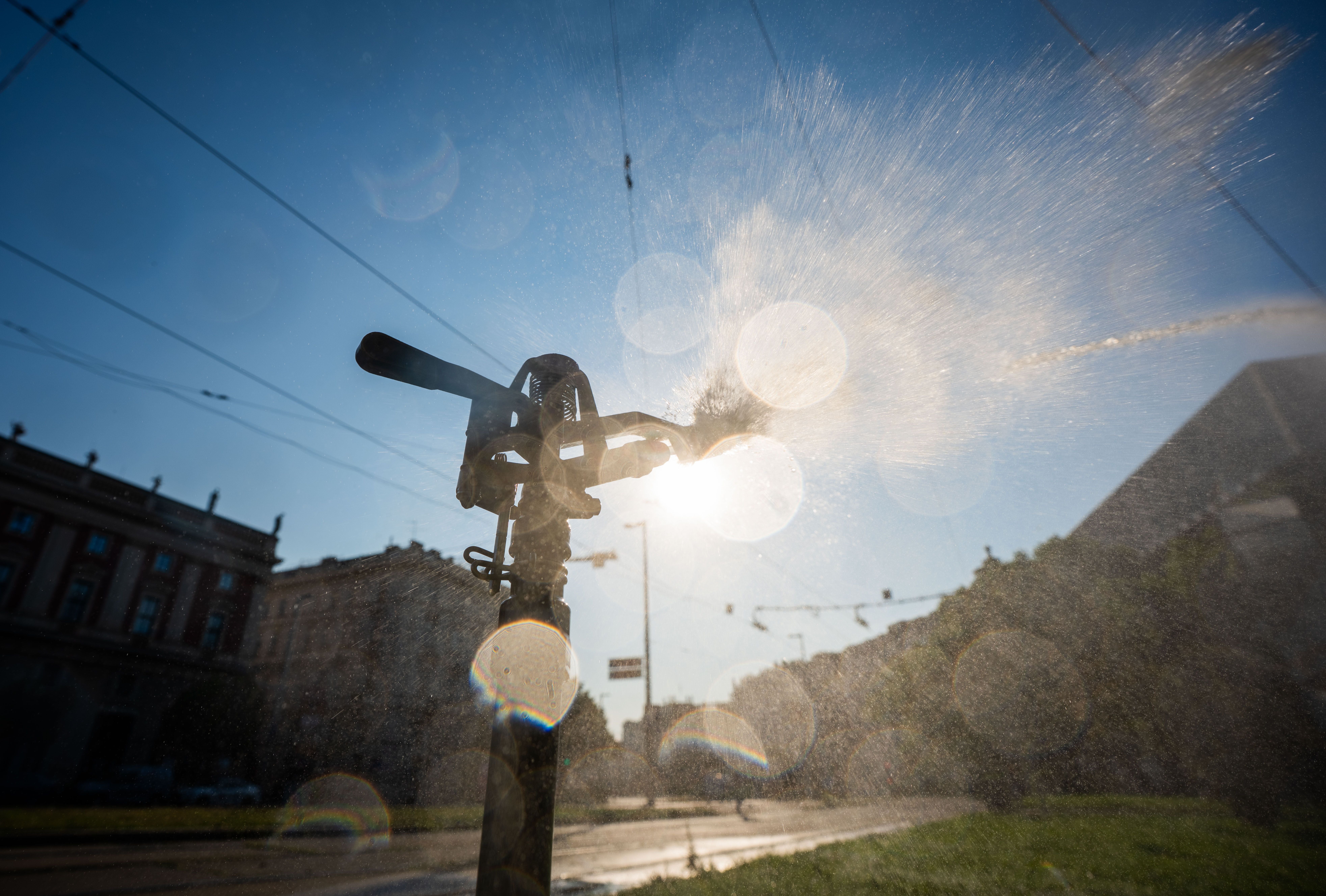 Ein Wassersprenger sprüht Wasser in einer Parkanlage bei Sonne am Karlsplatz in Wien.