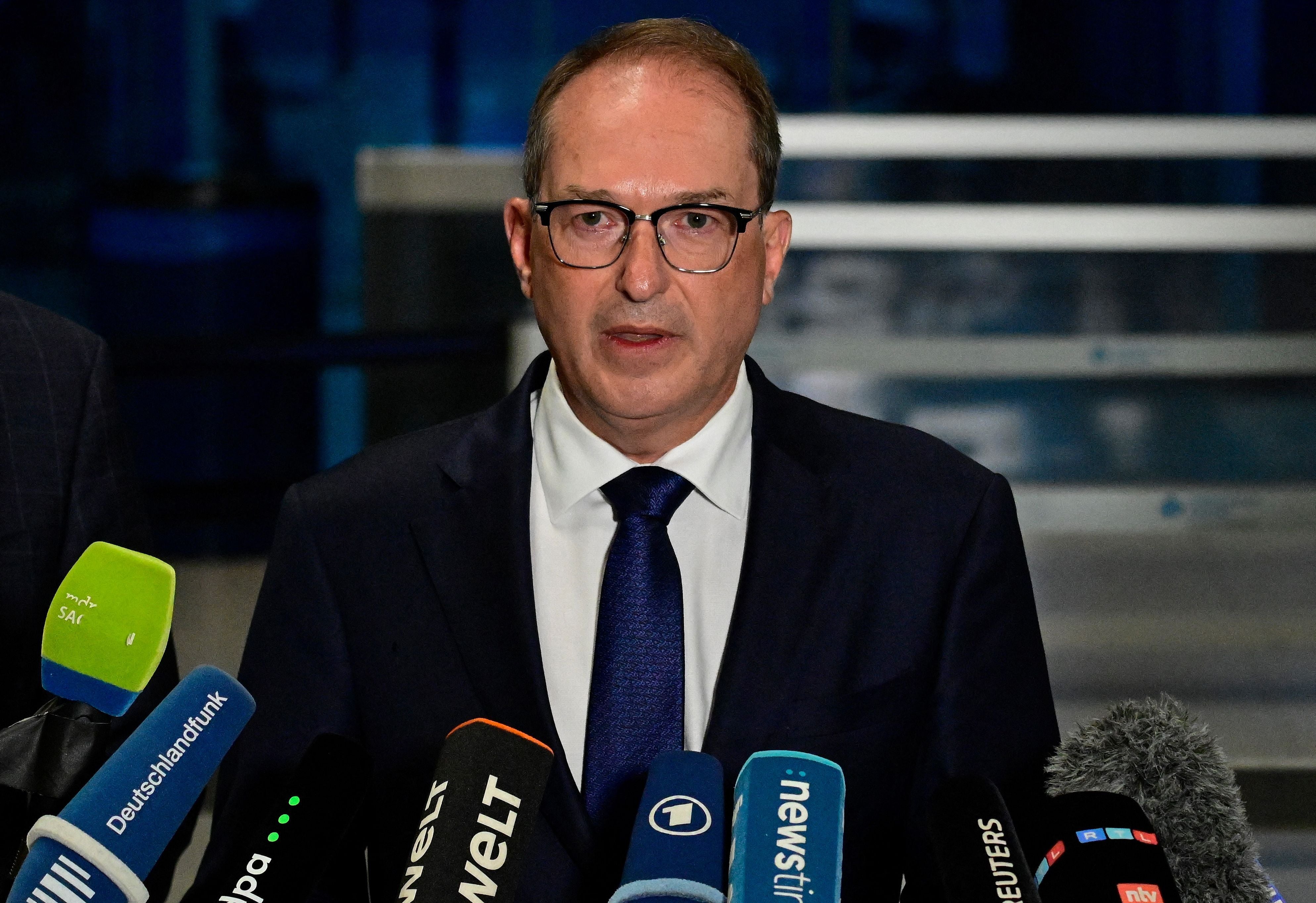 Ein Mann im Anzug spricht bei einer Pressekonferenz vor mehreren Mikrofonen.