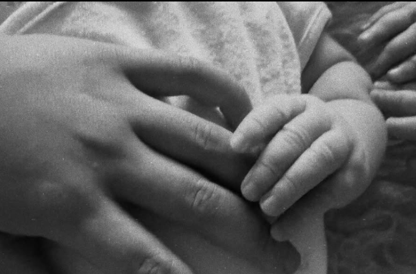 Eine Babyhand greift nach den Fingern einer erwachsenen Hand in Schwarzweiß.