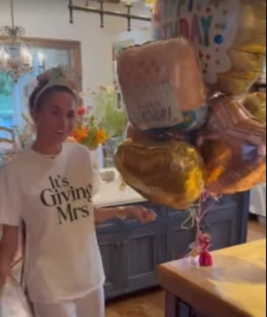 Frau mit Krone steht neben Geburtstagsballons in einer hellen Küche.