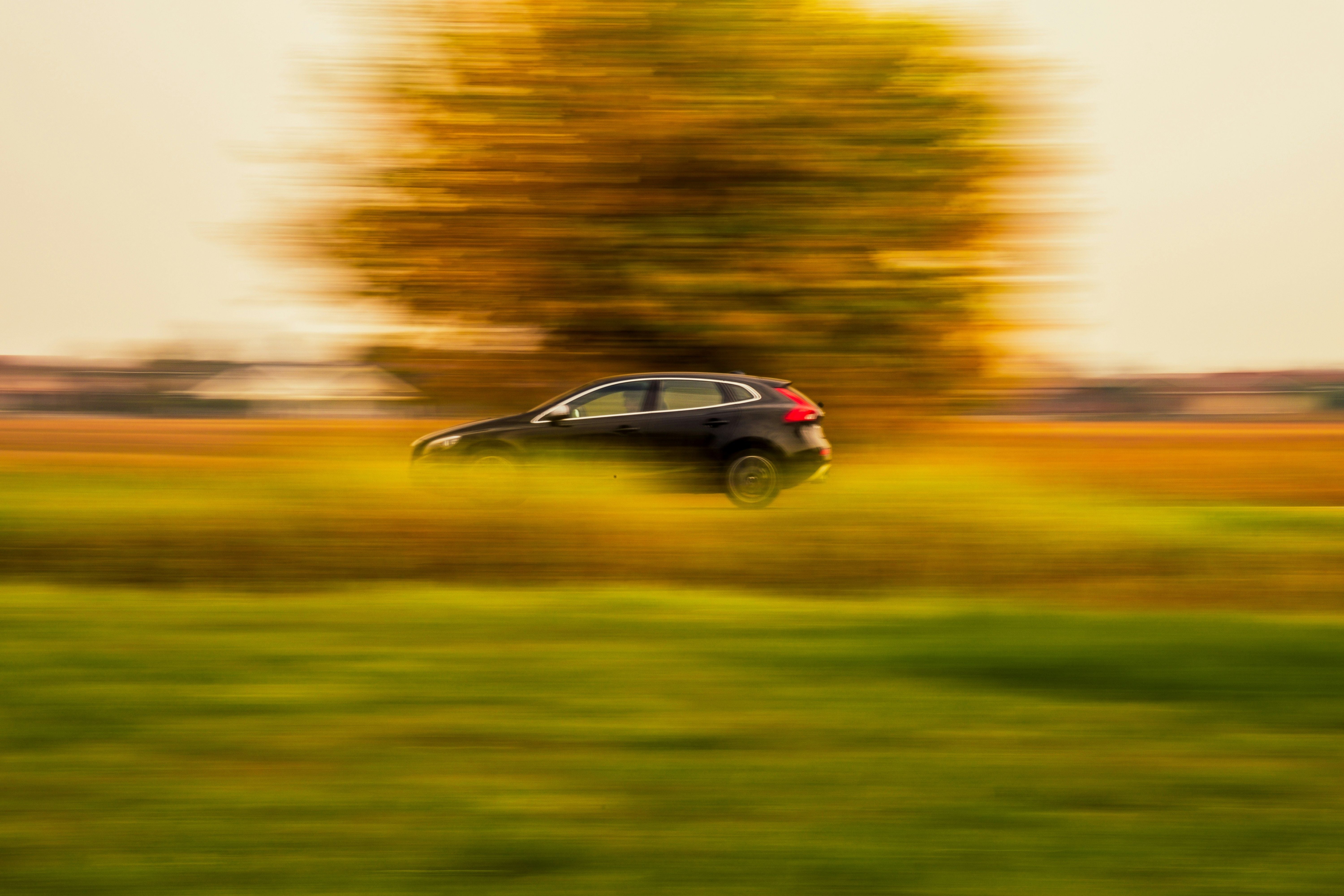 Schwarzes Auto fährt mit hoher Geschwindigkeit durch eine unscharfe, ländliche Landschaft.