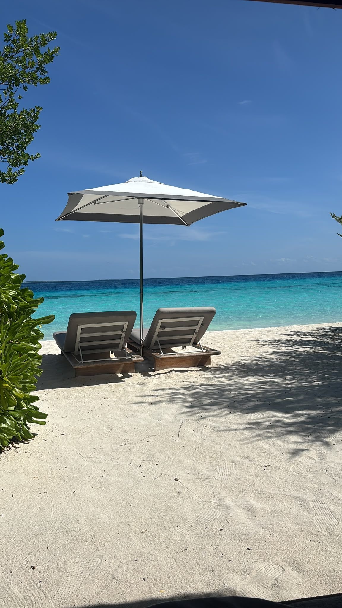 Zwei Liegestühle mit Sonnenschirm am weißen Sandstrand vor türkisblauem Meer.