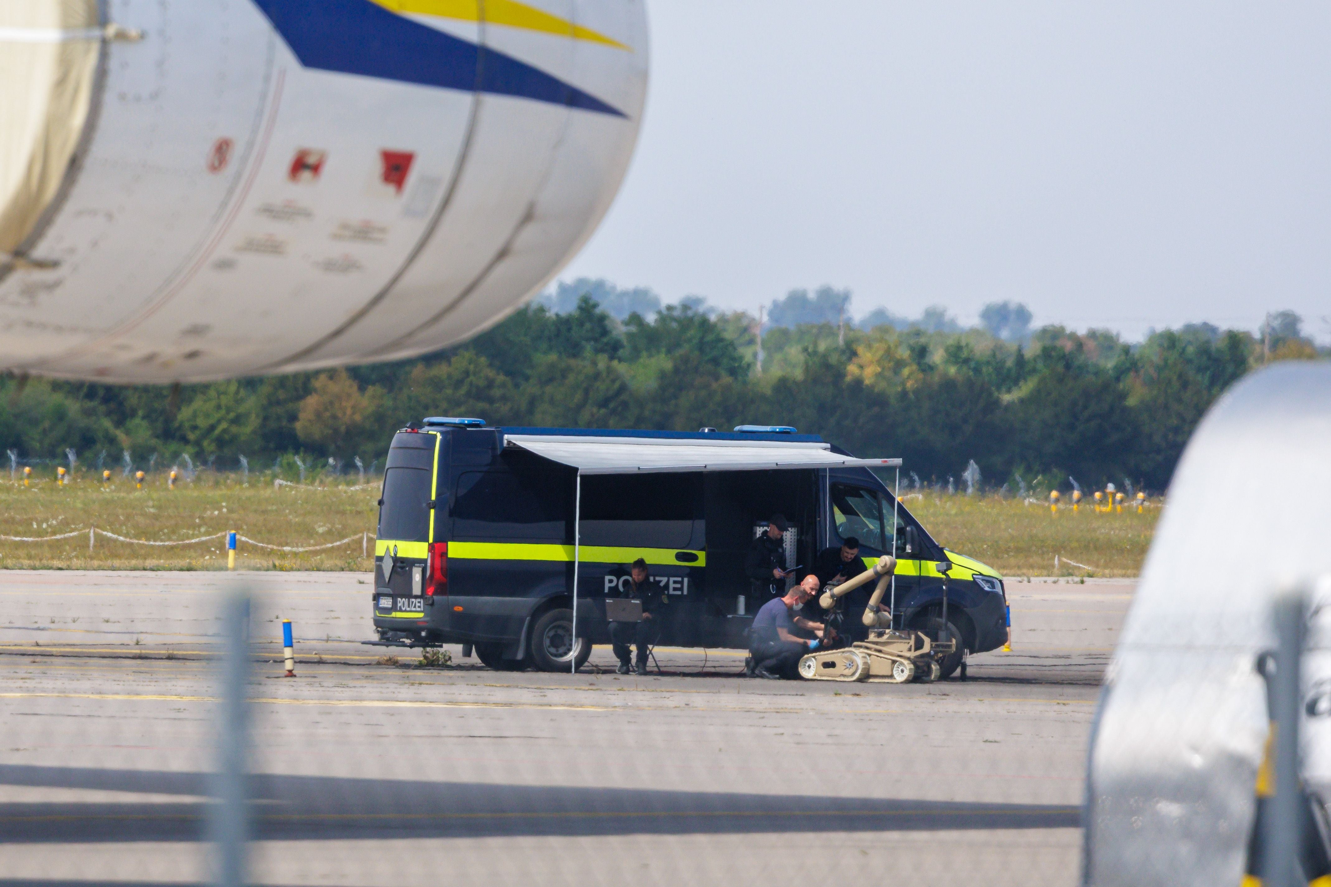 Polizisten arbeiten mit einem Entschärfungsroboter neben einem Polizeibus auf dem Flughafenvorfeld.