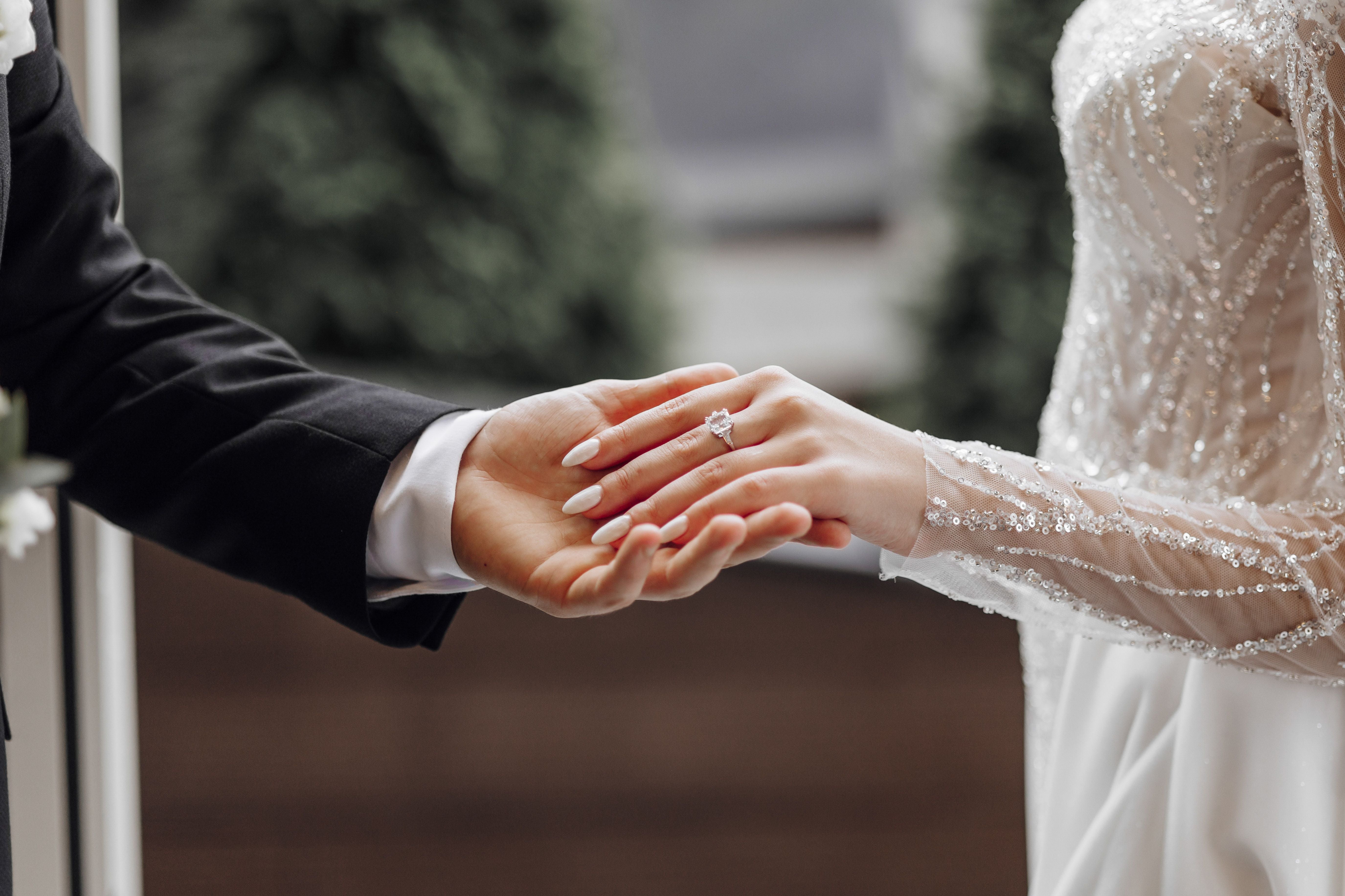 Bräutigam hält die Hand der Braut mit Ehering; Nahaufnahme bei einer Hochzeit.