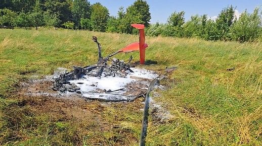 Verbranntes Wrack eines Kleinflugzeugs mit Schaum umgeben auf einer Wiese.