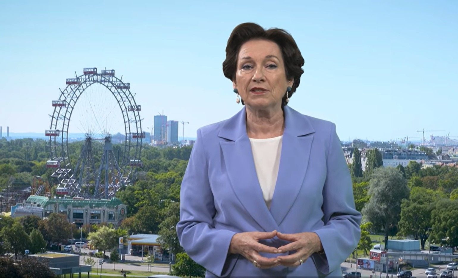Frau im blauen Blazer steht vor dem Wiener Riesenrad bei sonnigem Wetter.