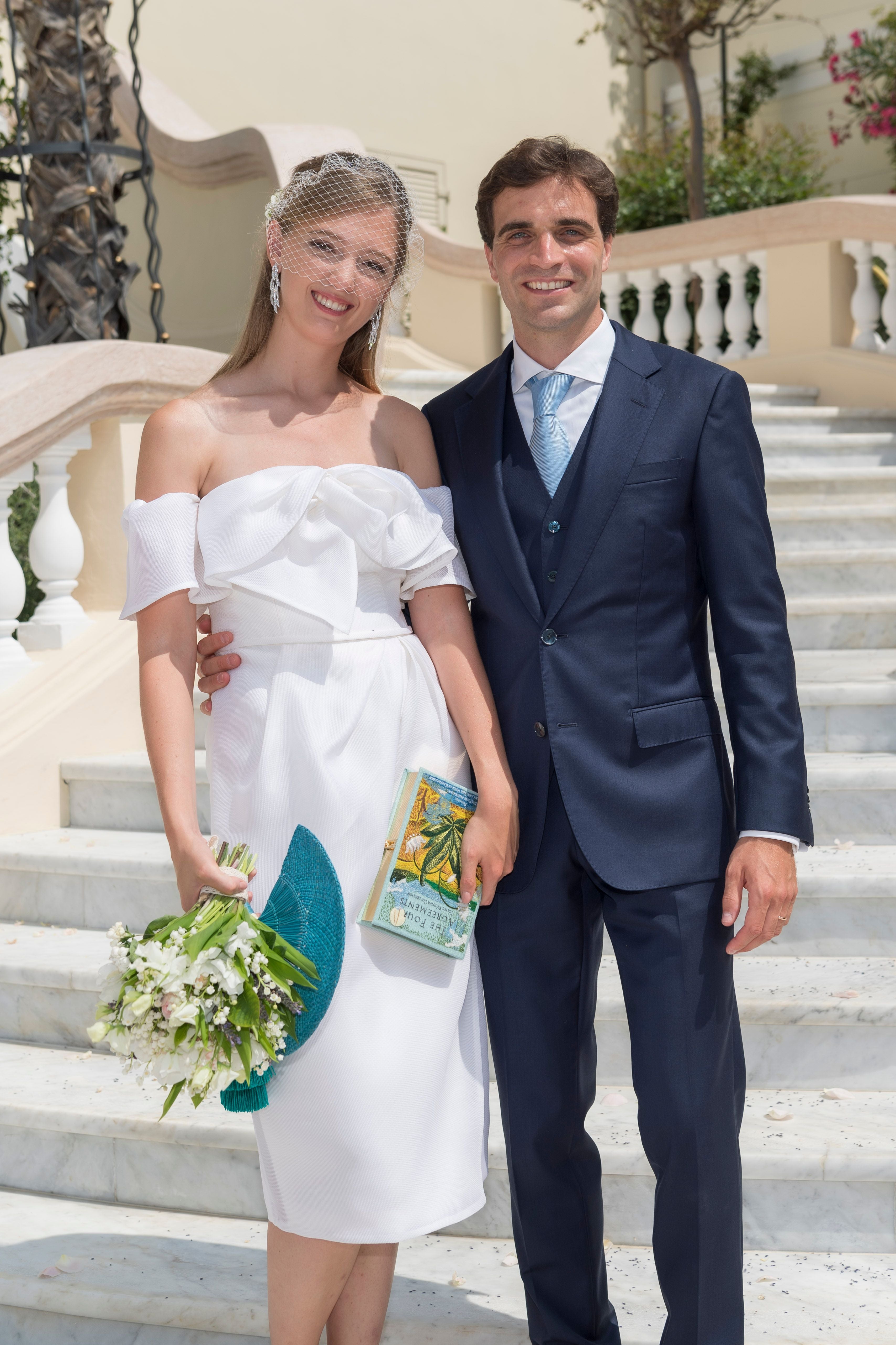 Ein Paar in eleganter Hochzeitskleidung steht lächelnd auf Marmortreppen im Freien.