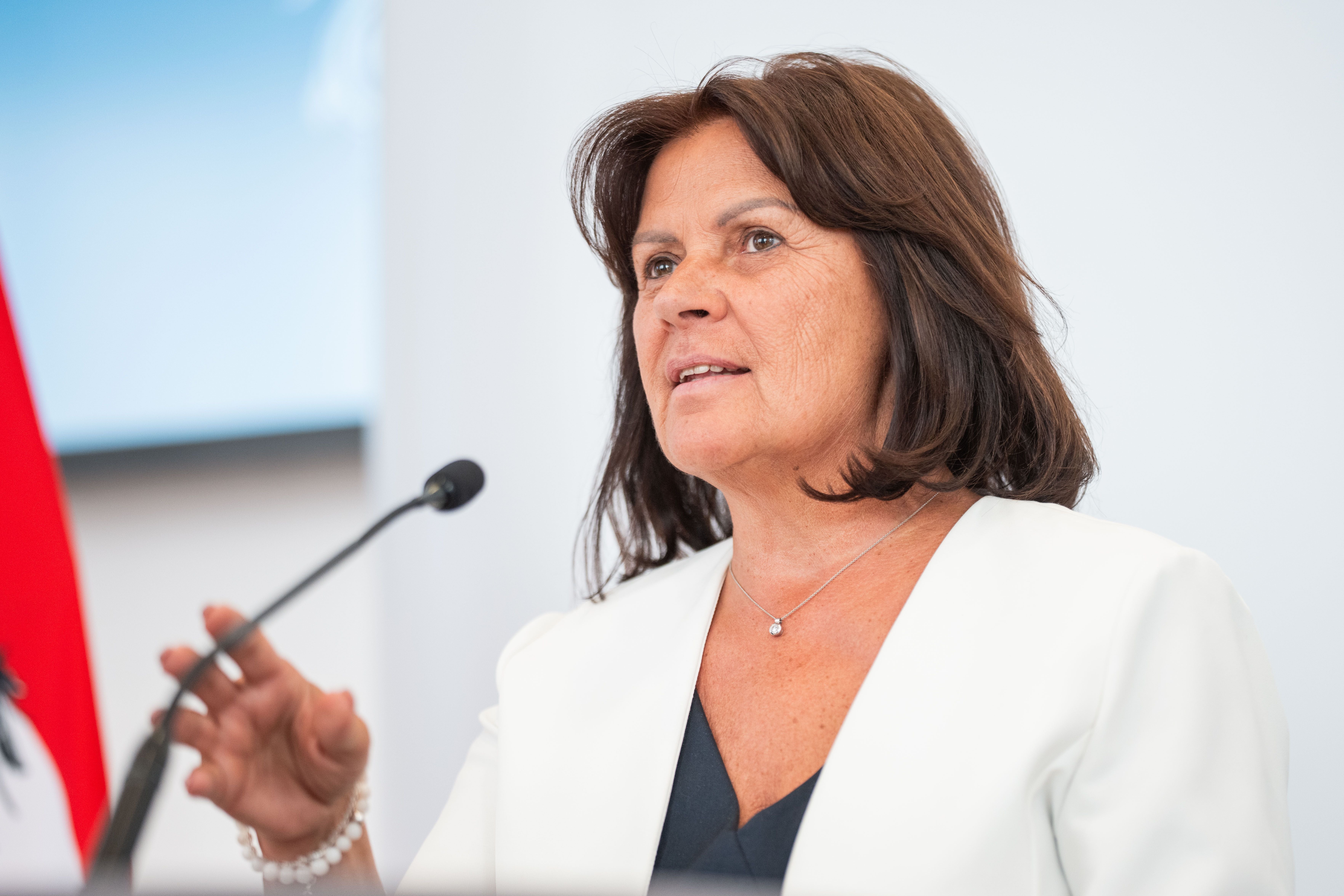 Eine Frau spricht bei einer Pressekonferenz am Mikrofon, Hintergrund neutral.