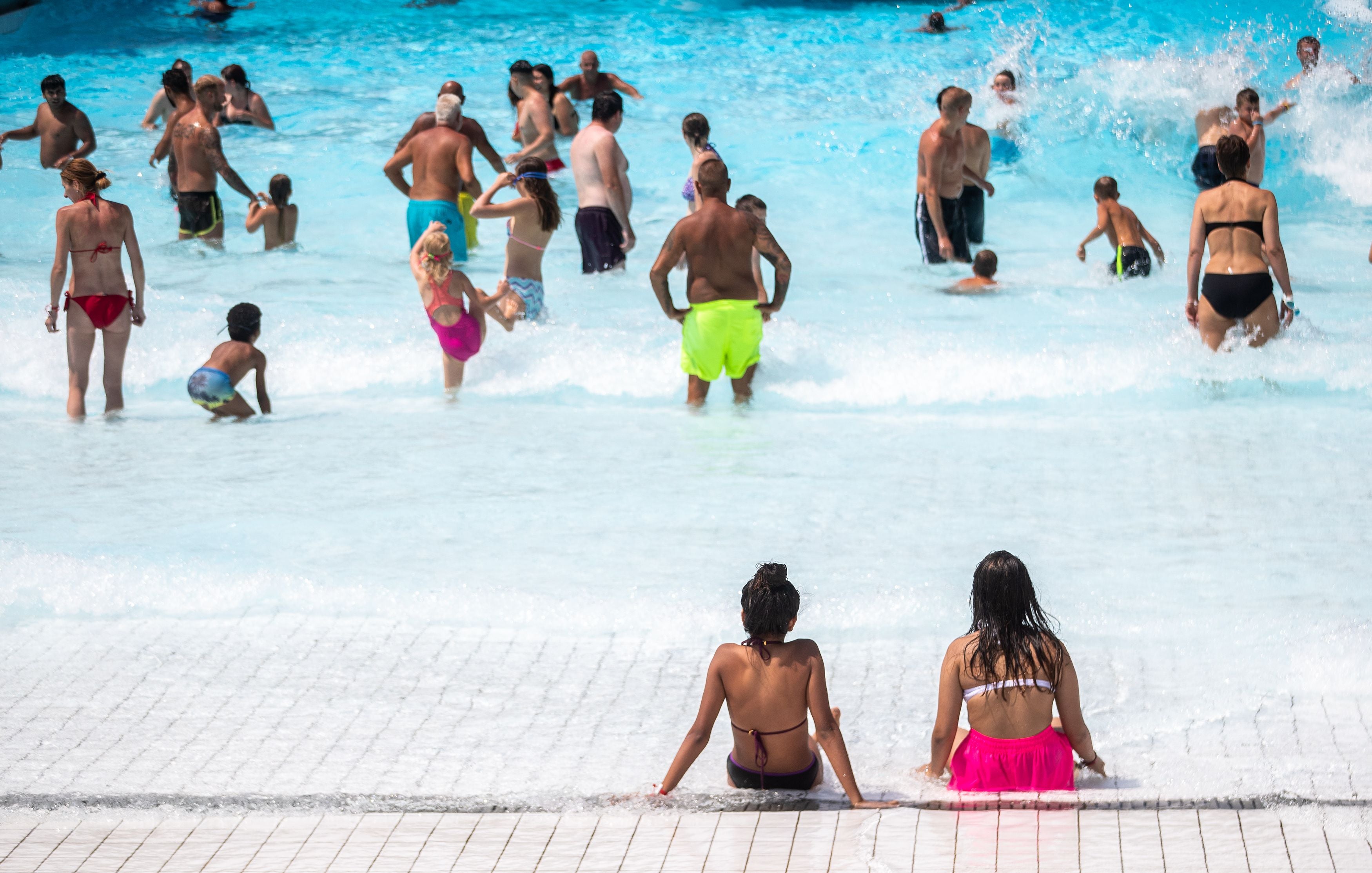 Viele Menschen baden und entspannen sich im sonnigen Wellenbecken eines Freibads.