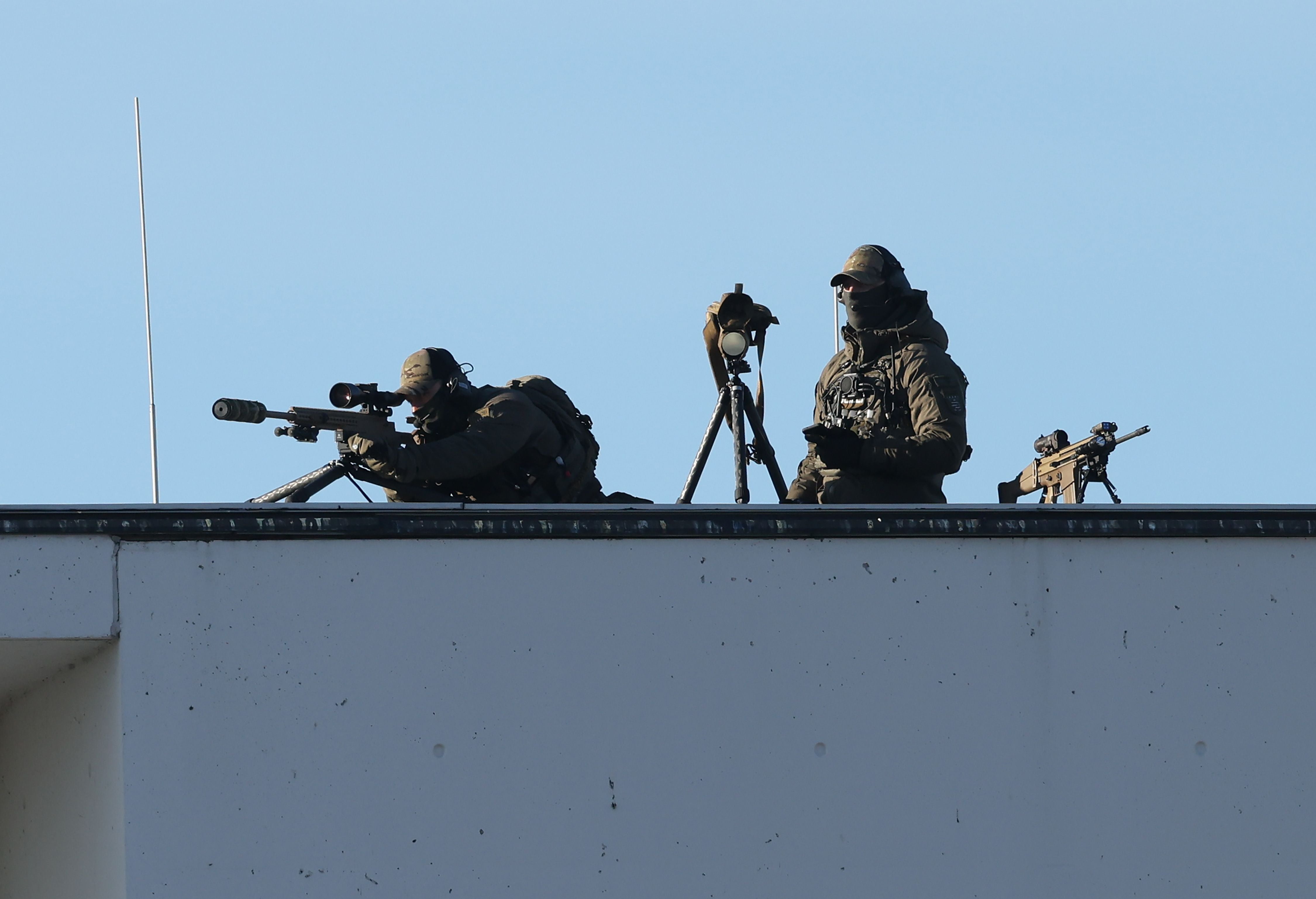 Zwei Polizeischarfschützen stehen mit Ausrüstung auf dem Dach eines Gebäudes.