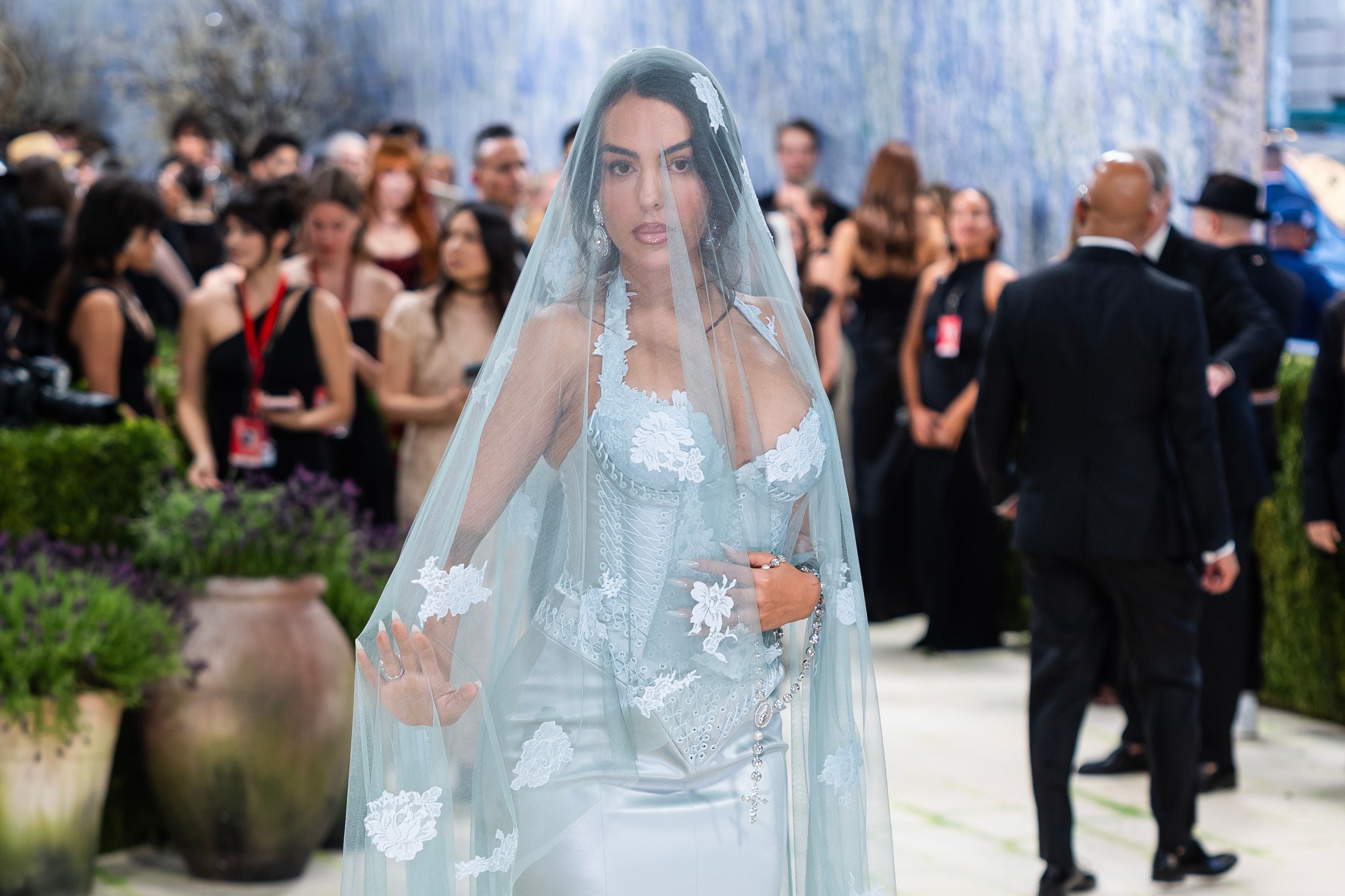 Eine Frau im weißen, bestickten Kleid und Schleier steht elegant auf einem Gala-Event.