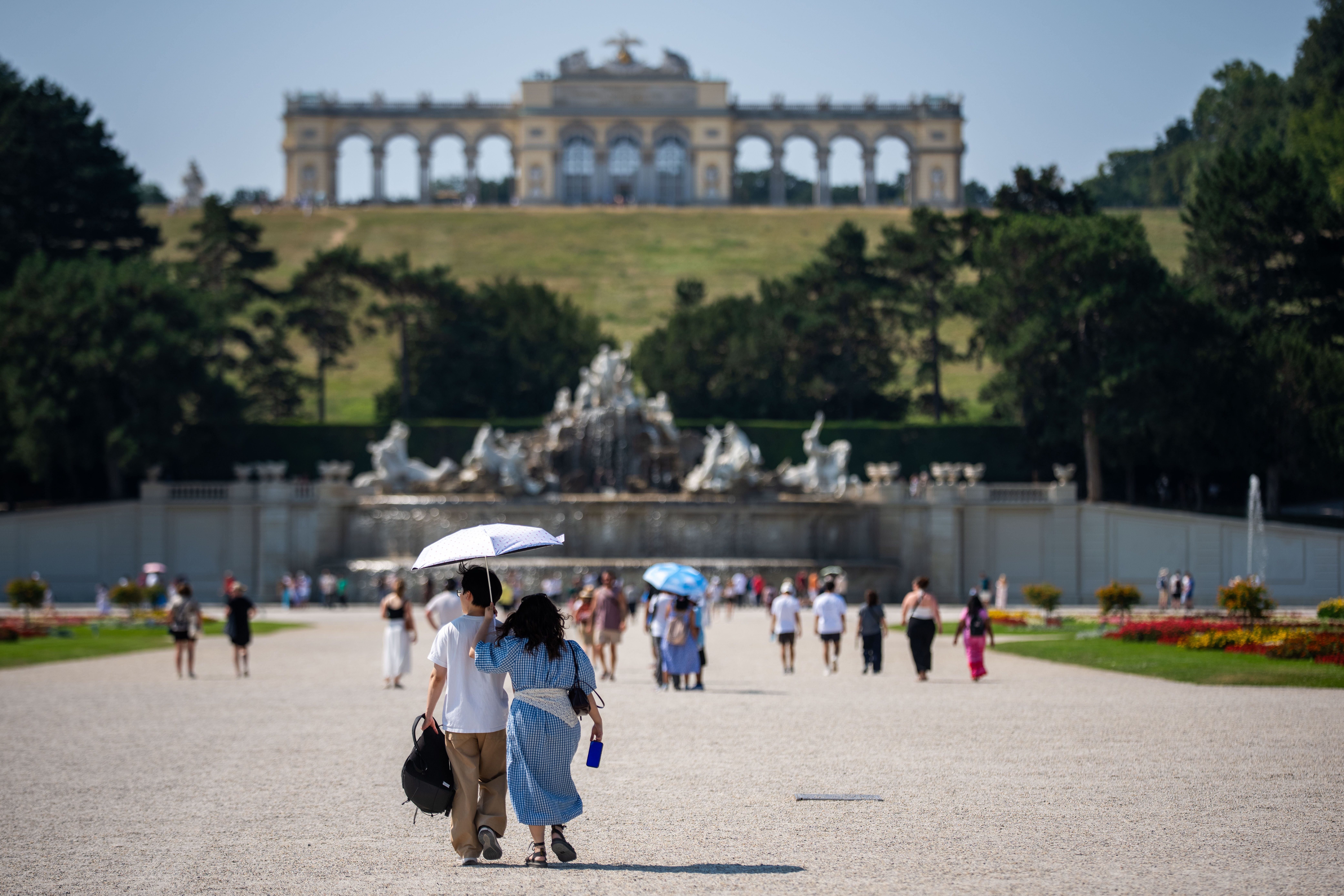 Touristen im Schlosspark Schönbrunn schützen sich mit Schirmen vor der Sonne bei Hitze.