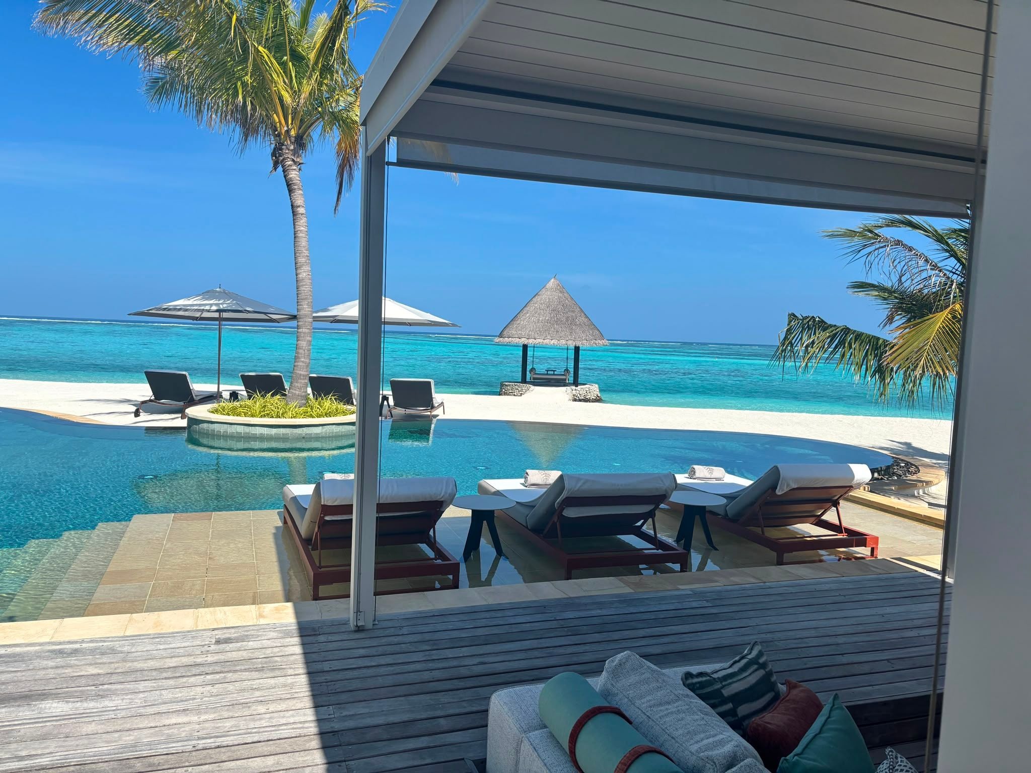 Luxuriöse Villa mit Pool, Liegen, Palmen und Blick auf das blaue Meer und einen Sandstrand.