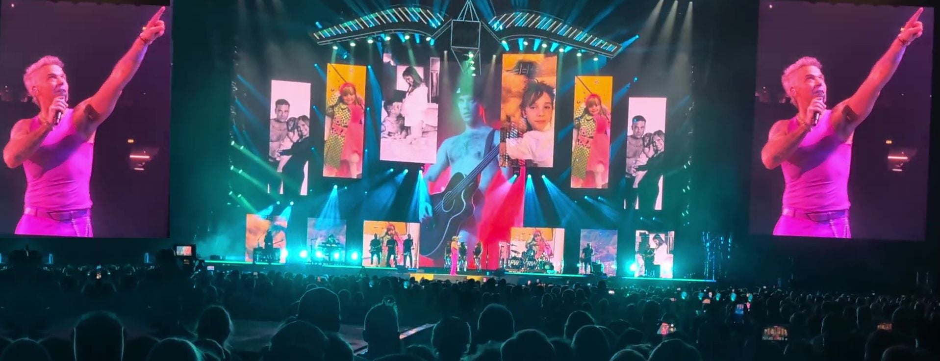 Robbie Williams singt auf einer großen, bunt beleuchteten Konzertbühne vor großem Publikum.